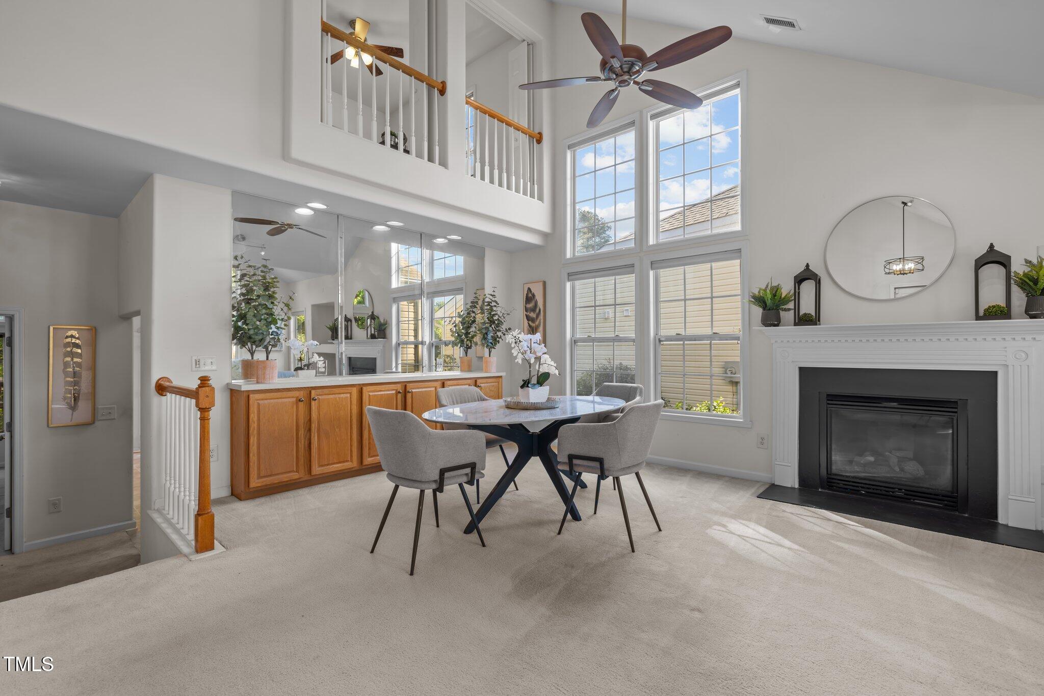 Dining area with a round table beside a fireplace and tall windows beneath a two-story ceiling.