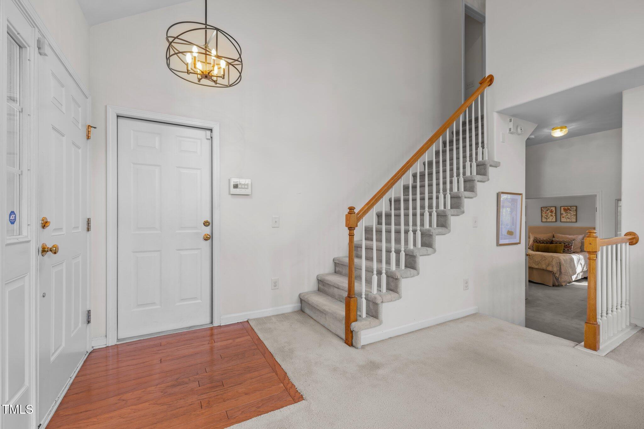 Entry foyer with a carpeted staircase, wood handrail, hardwood floor, and chandelier.