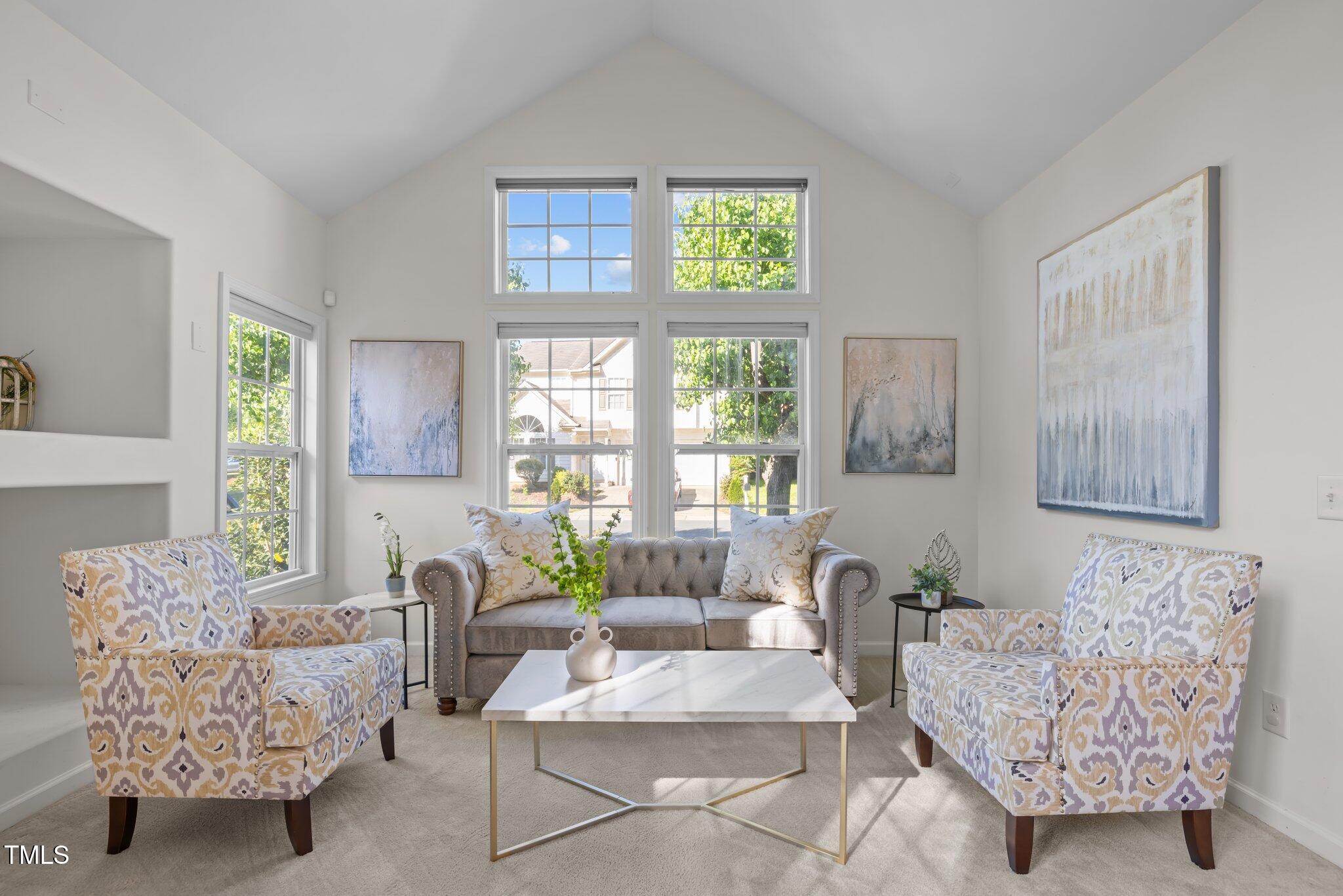 Living room with vaulted ceiling, tall windows, gray sofa, and patterned armchairs.