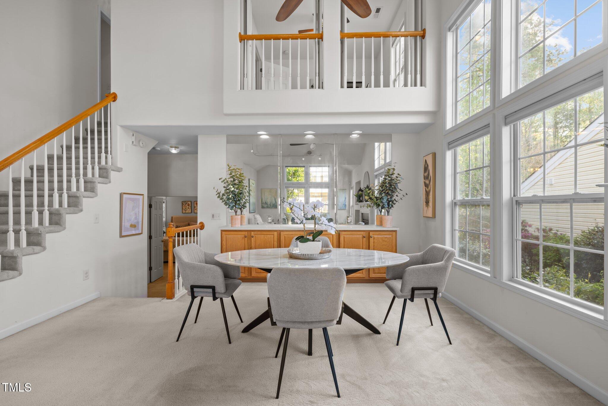 Dining area with a round table, tall windows, carpeted stairs, and an open loft above.