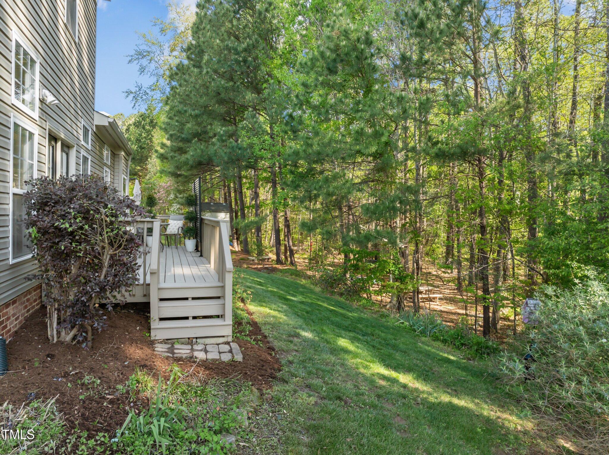 House deck overlooks a sloping grassy backyard and mature trees.