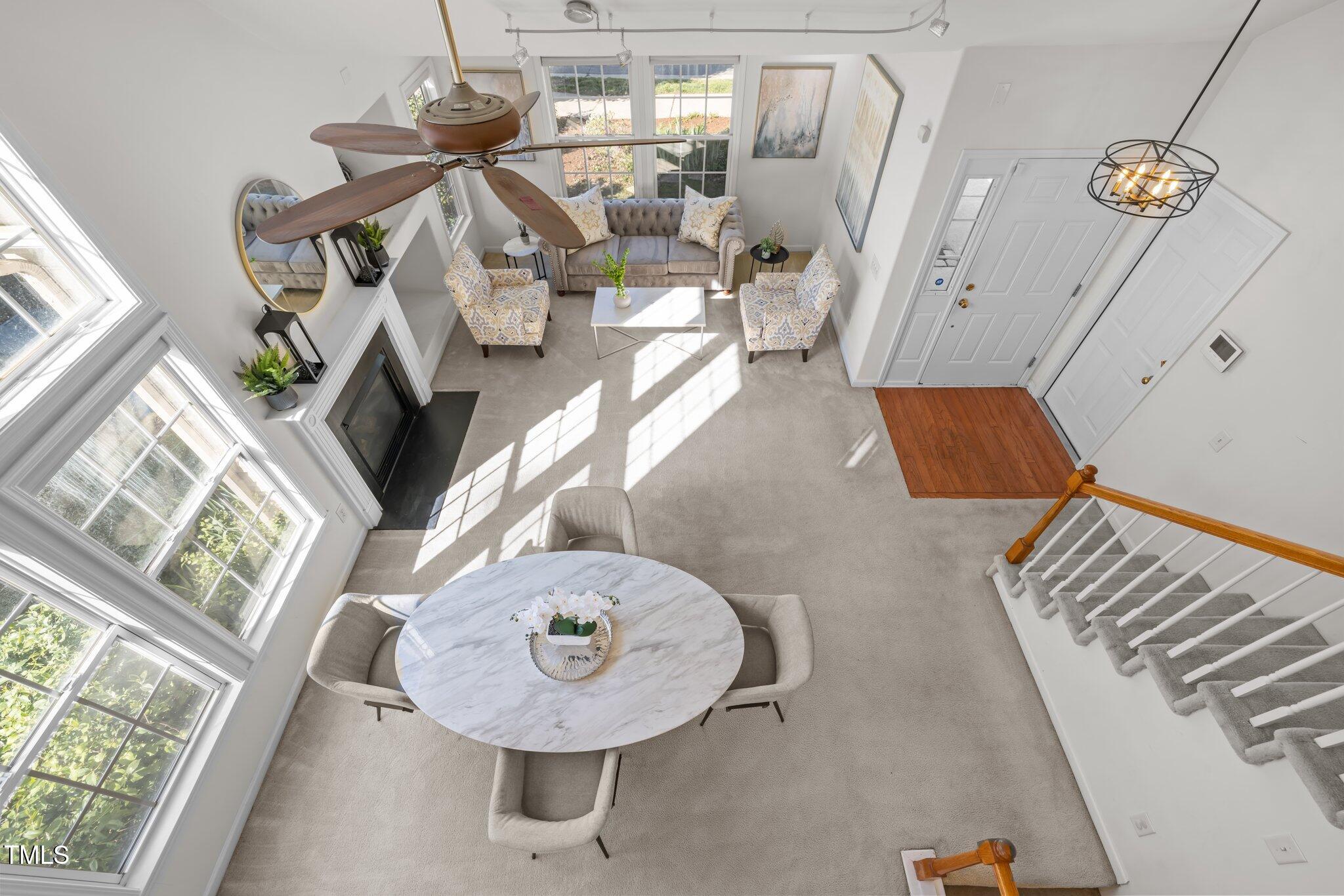 Overhead view of a furnished living room with tall windows, fireplace, dining table, and staircase.