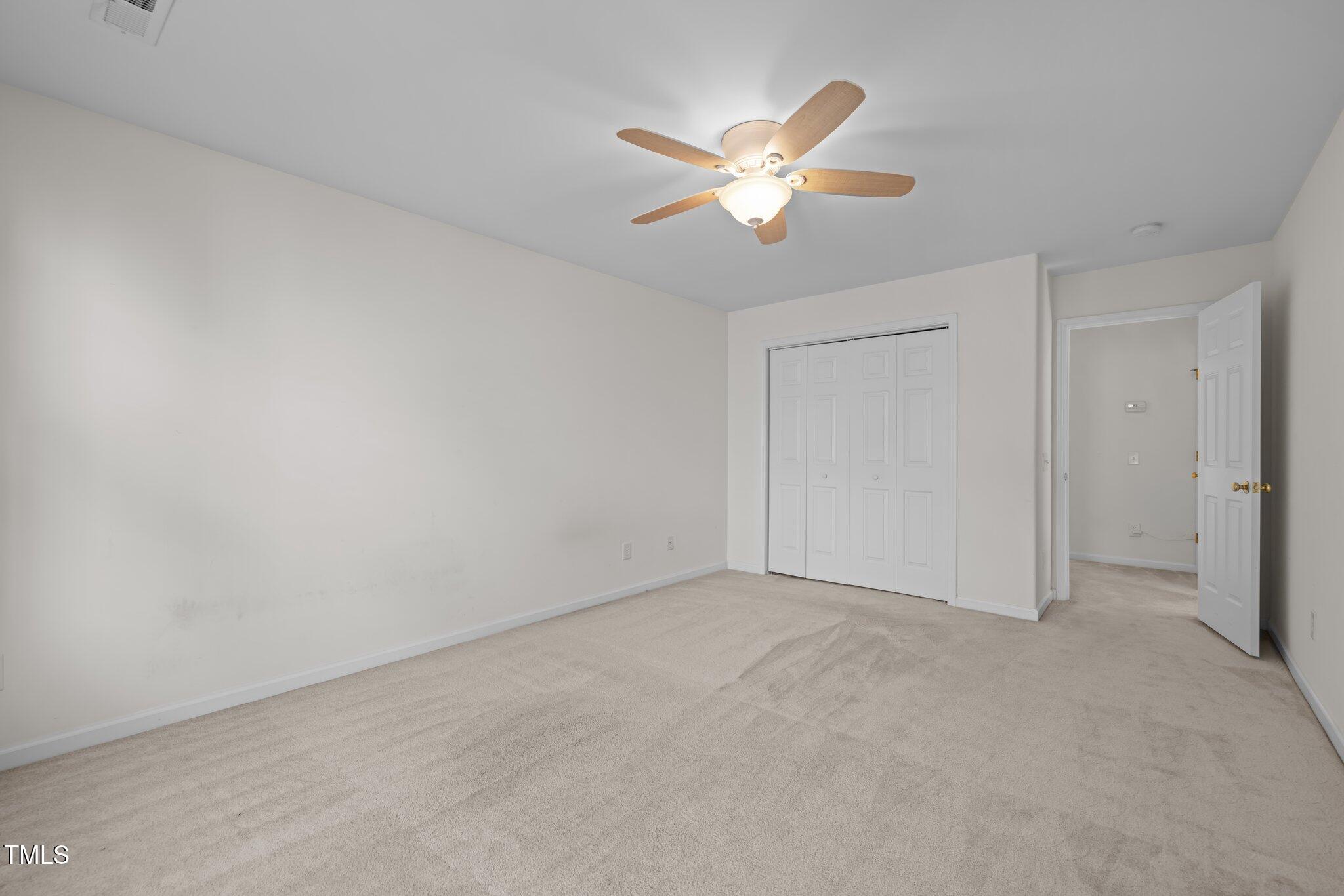 Empty carpeted bedroom with a ceiling fan, closet doors, and an open doorway.