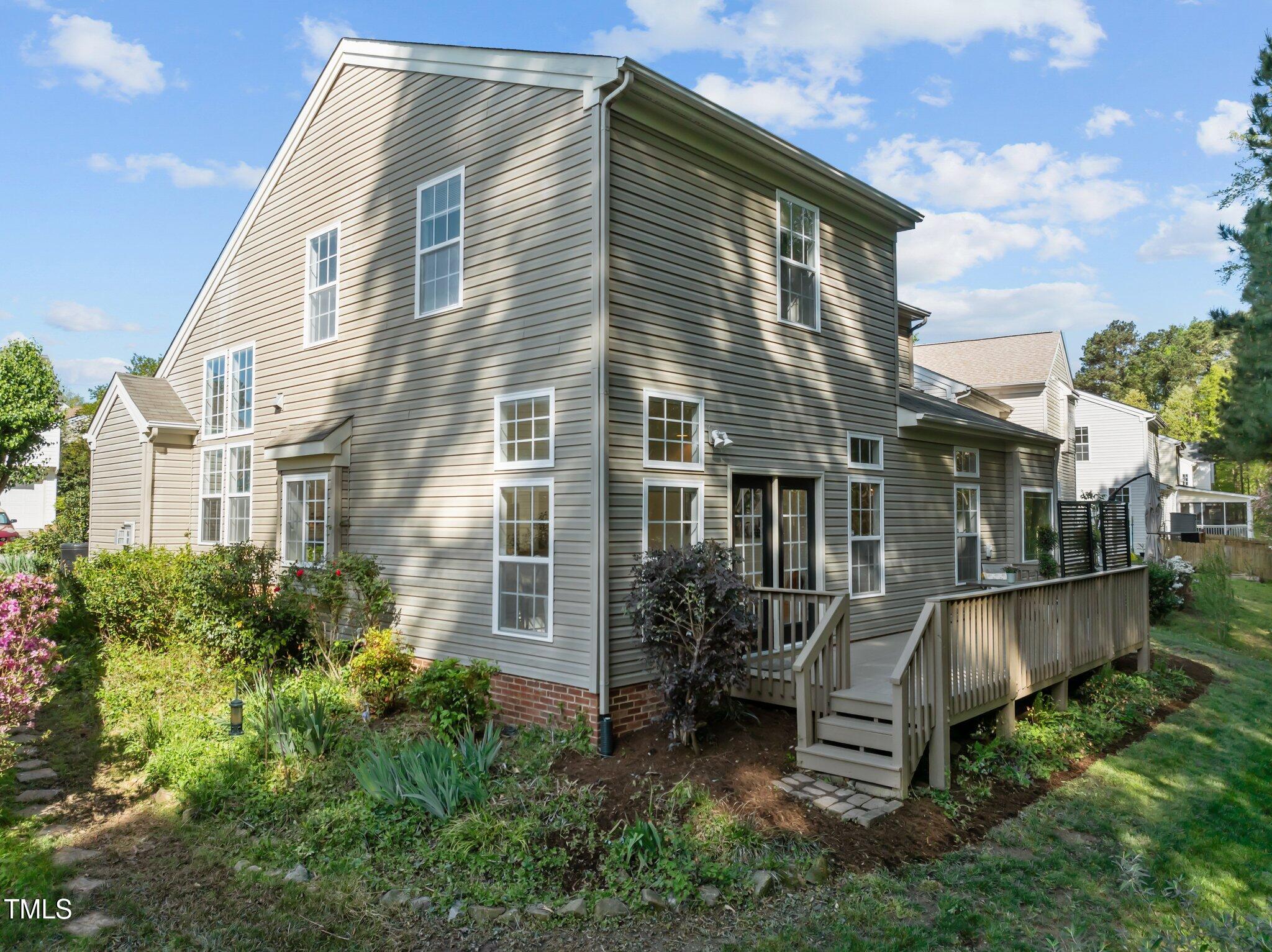 Two-story home with a raised wooden deck, wide steps, and landscaped garden beds.