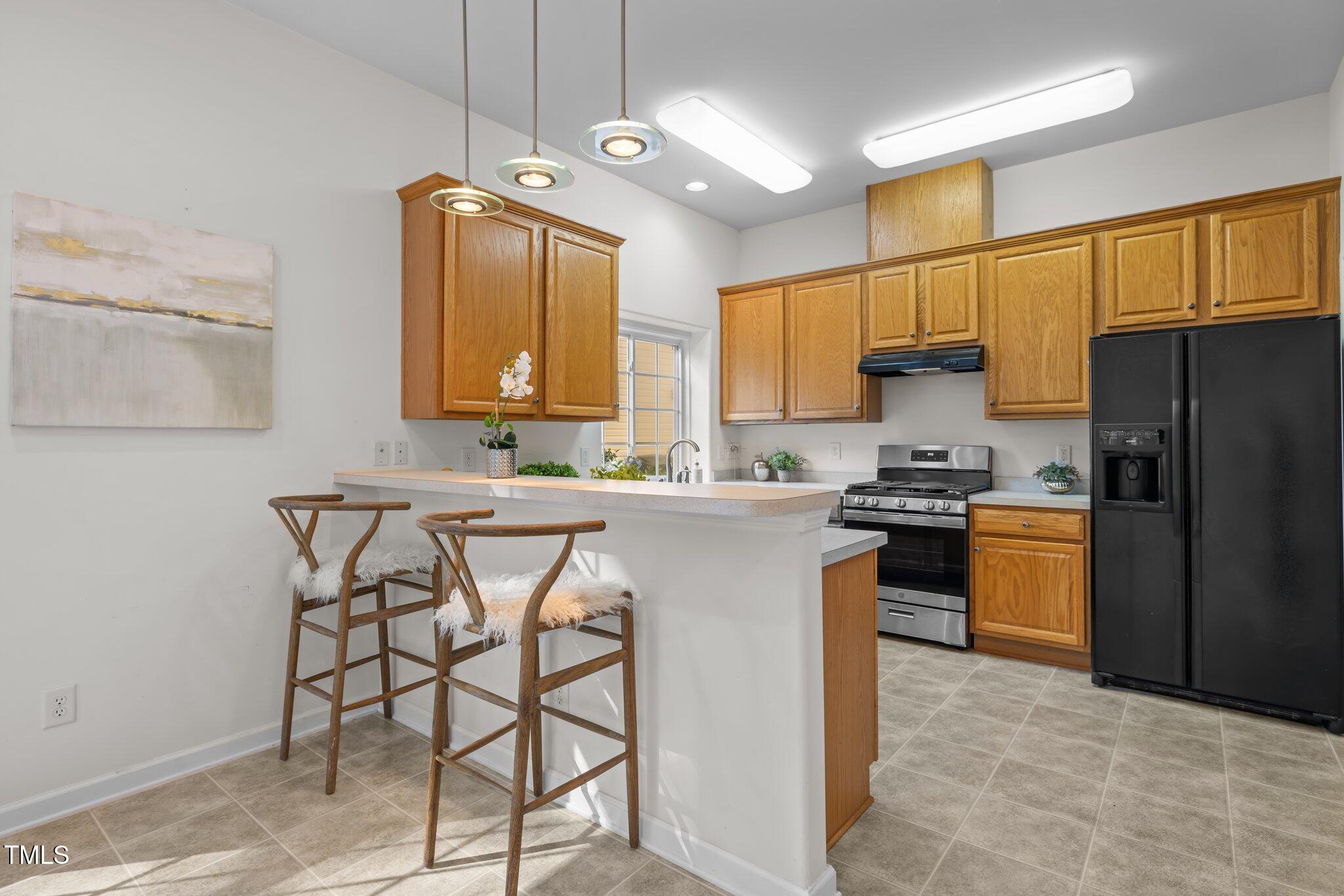 Kitchen with honey-colored cabinets, a white peninsula, two bar stools, and stainless steel range.