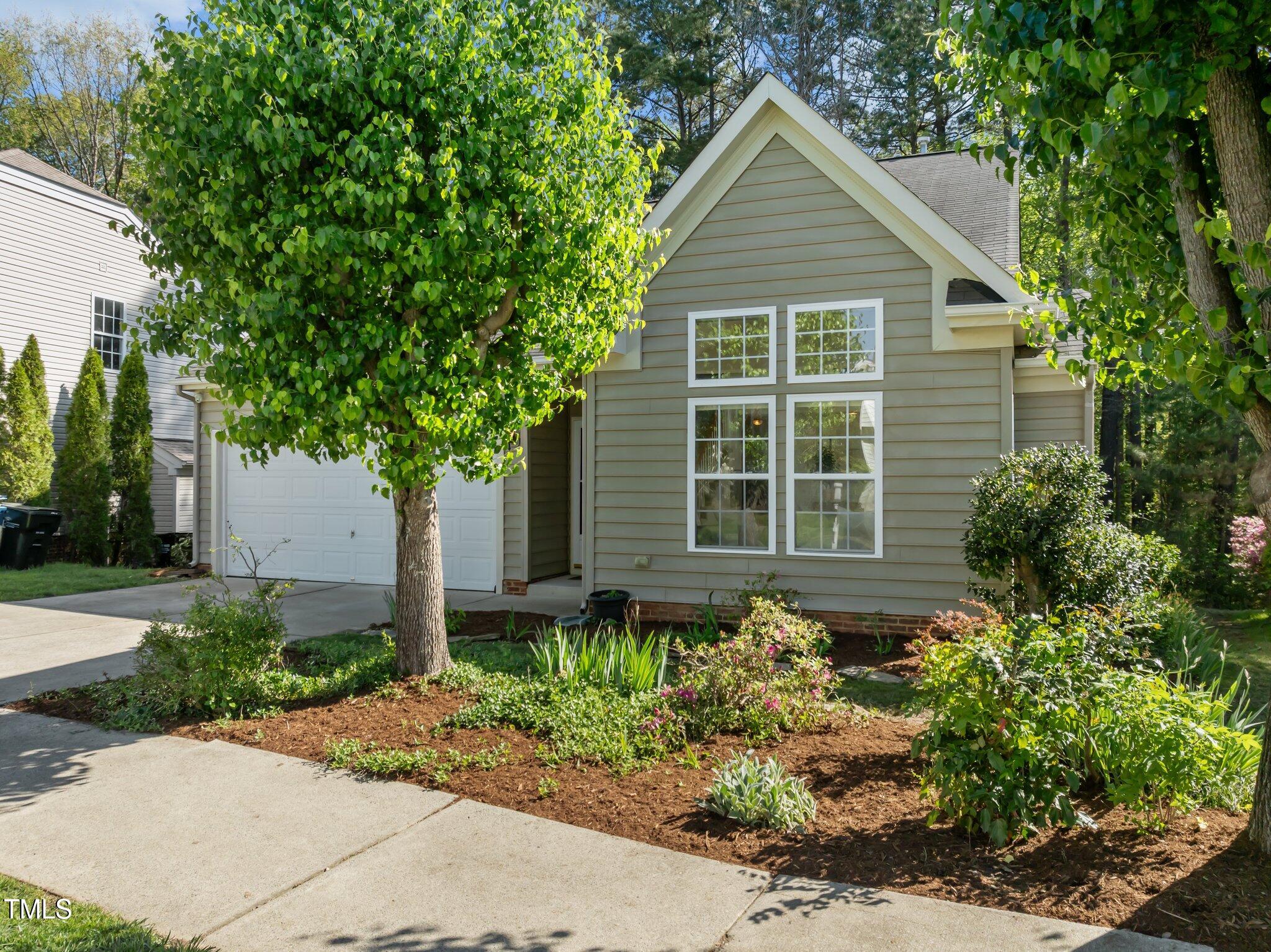 Gray-sided home with a front gable, white-trimmed windows, attached garage, and mature trees.
