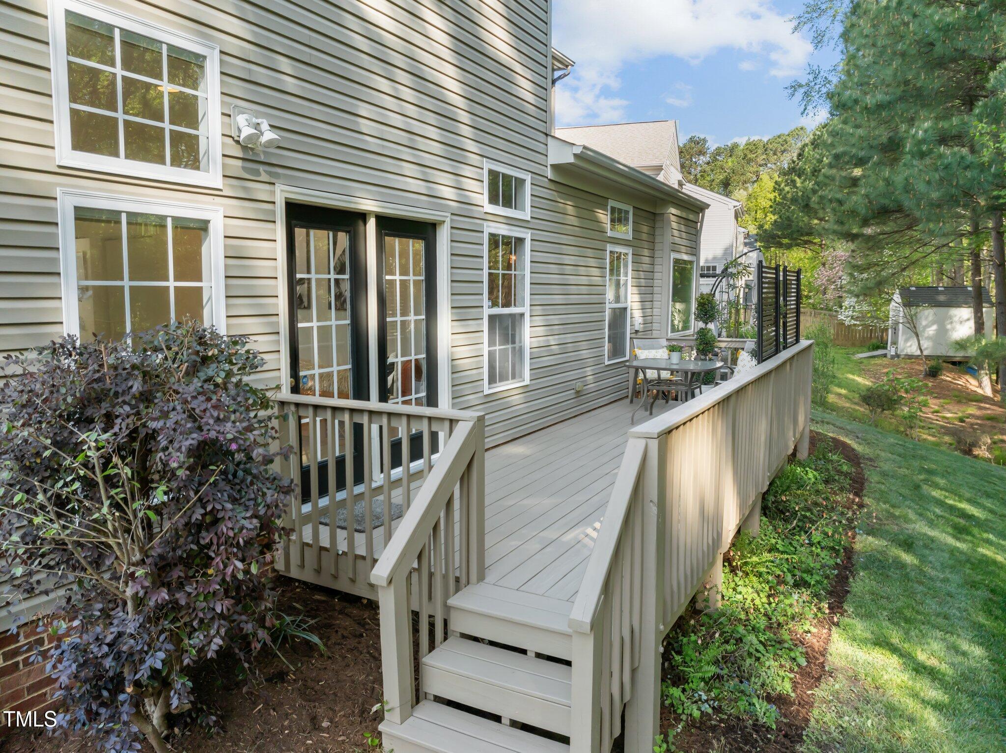 Raised rear deck with wide stairs, a patio dining set, and a leafy yard.