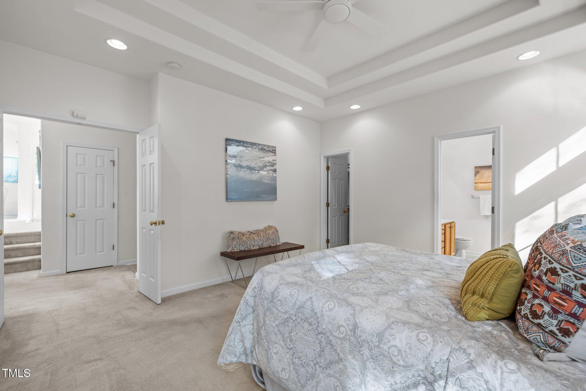 Furnished bedroom with a tray ceiling, ceiling fan, and adjoining bathroom doorway.