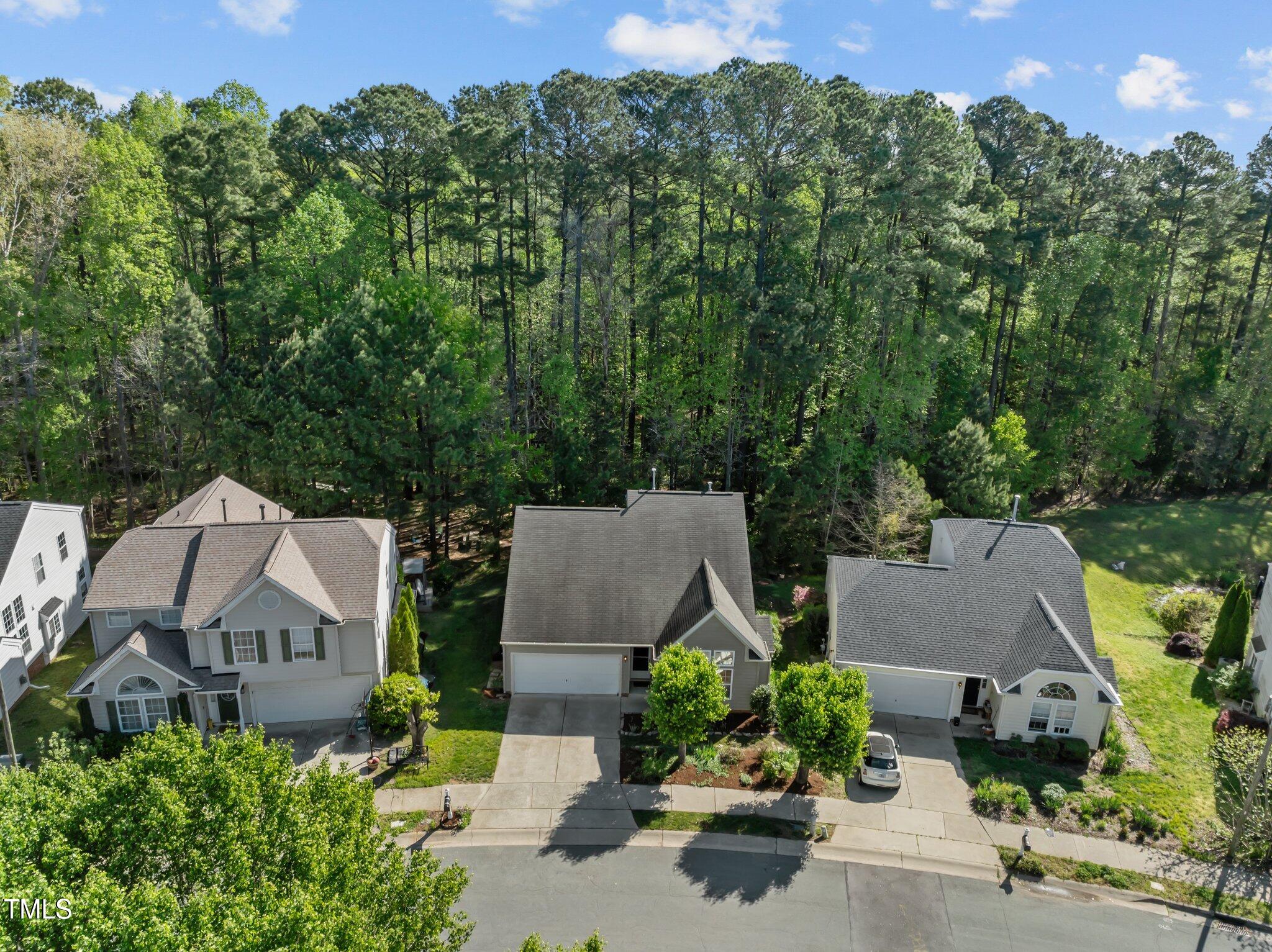 Aerial view of a home beside a wooded tree line and neighboring houses.