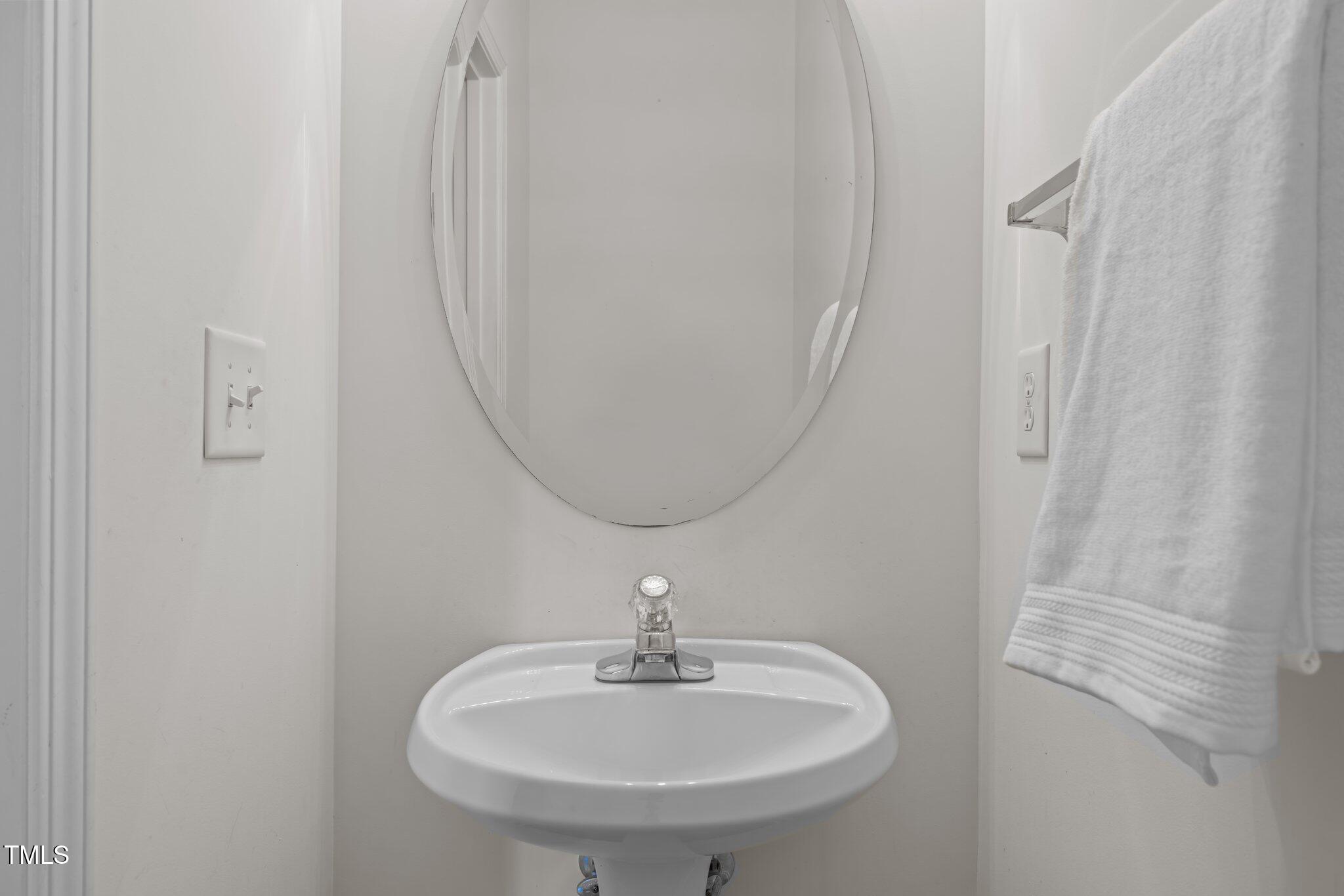 Bathroom sink beneath an oval mirror, with a white towel hanging beside it.