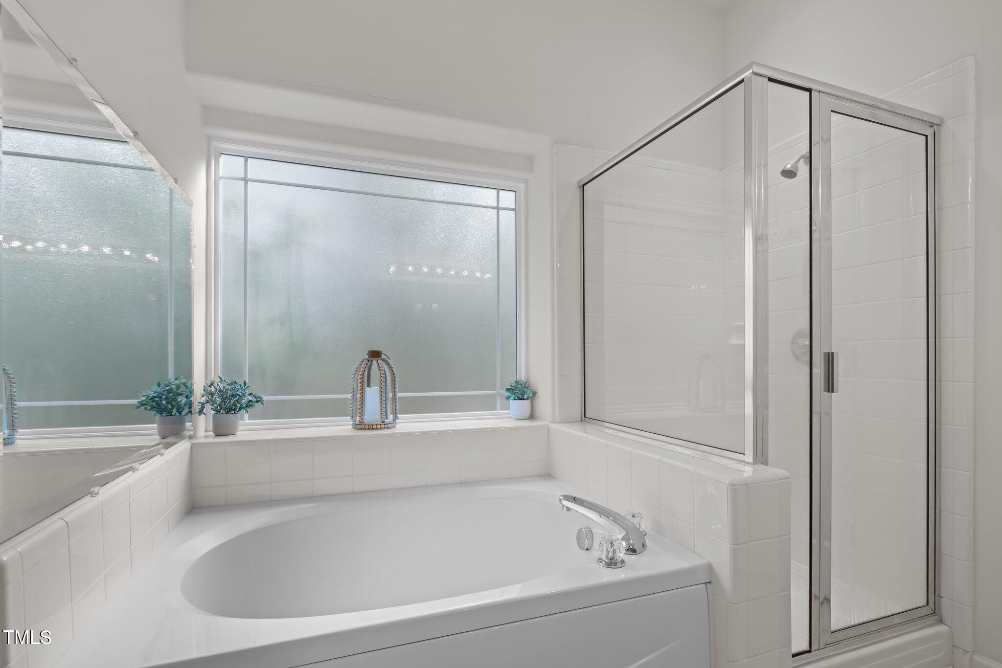 White soaking tub beneath a wide frosted window beside a glass-enclosed shower.