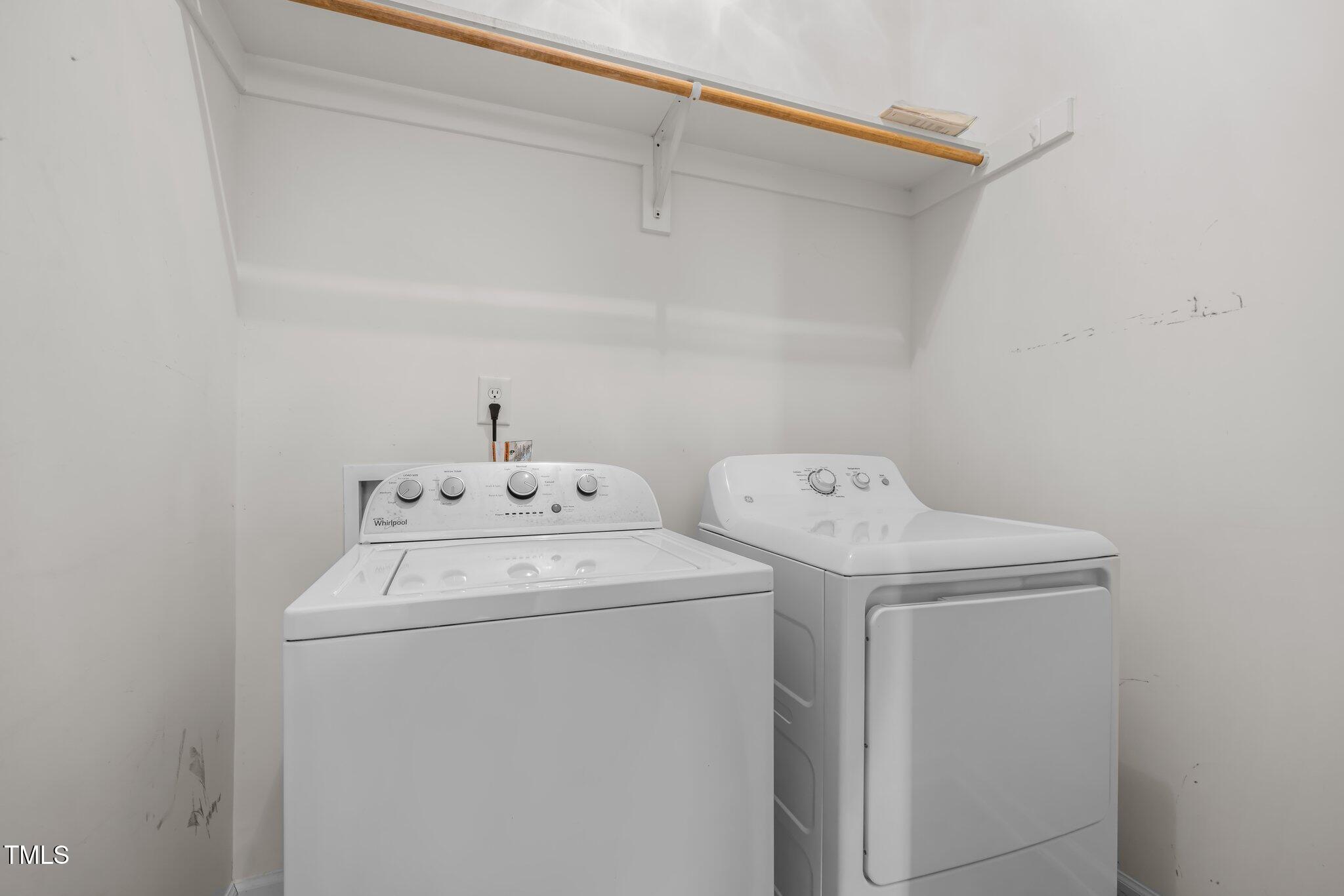 Laundry room with a white washer and dryer beneath a shelf and hanging rod.
