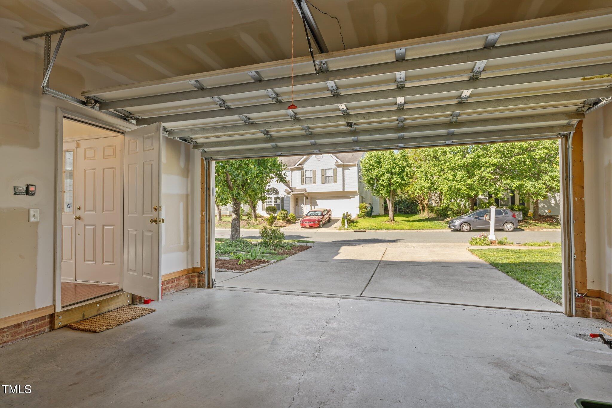 Open garage overlooking a concrete driveway and tree-lined residential street.