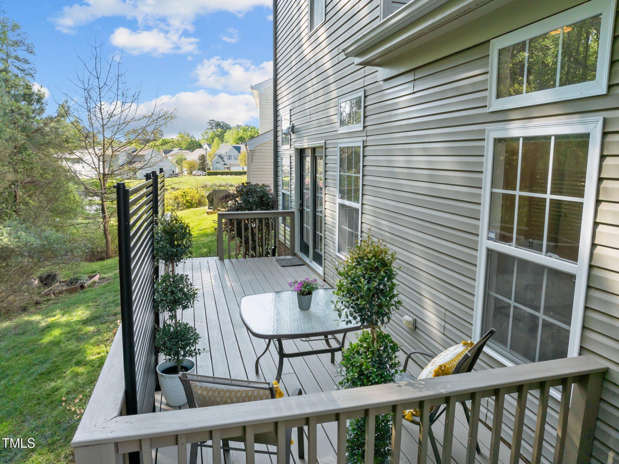 Rear deck with patio seating and potted shrubs overlooking a grassy backyard.