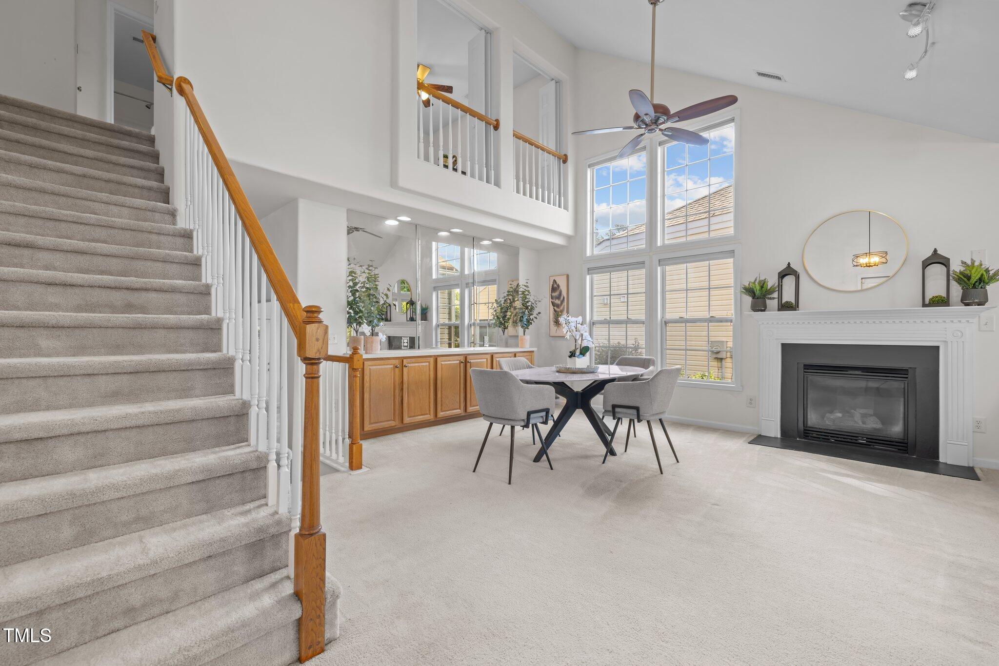 Living and dining room with a tall staircase, large windows, and a white fireplace.