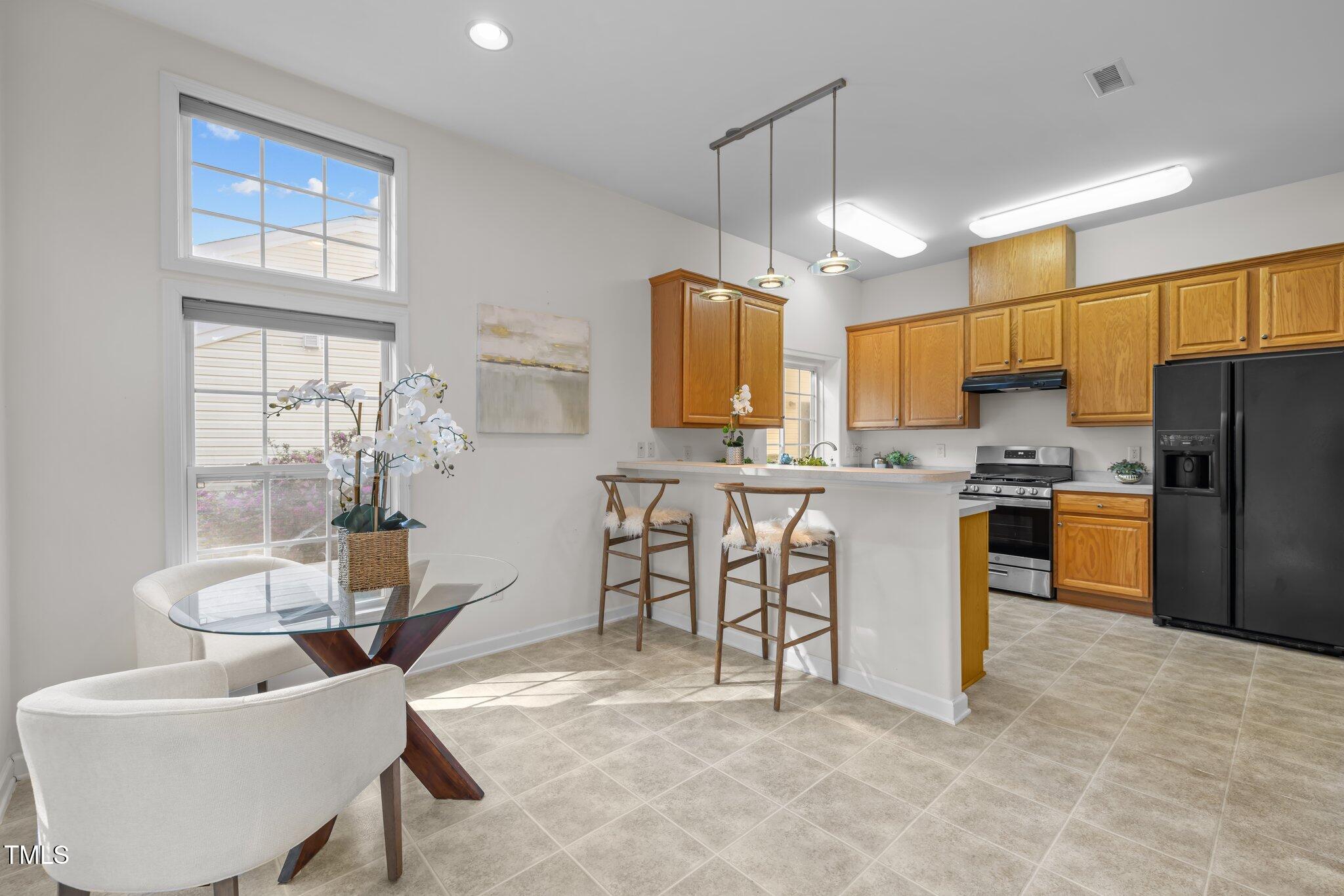 Kitchen and dining area with wood cabinets, breakfast bar, and glass table beside tall windows.