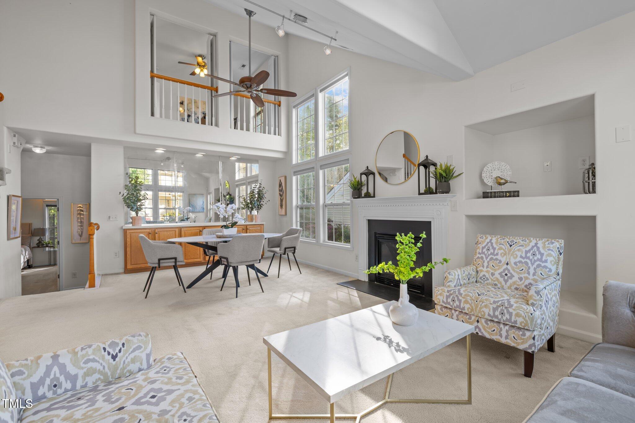 Open-plan living and dining room with a vaulted ceiling, tall windows, fireplace, and patterned accent chairs.