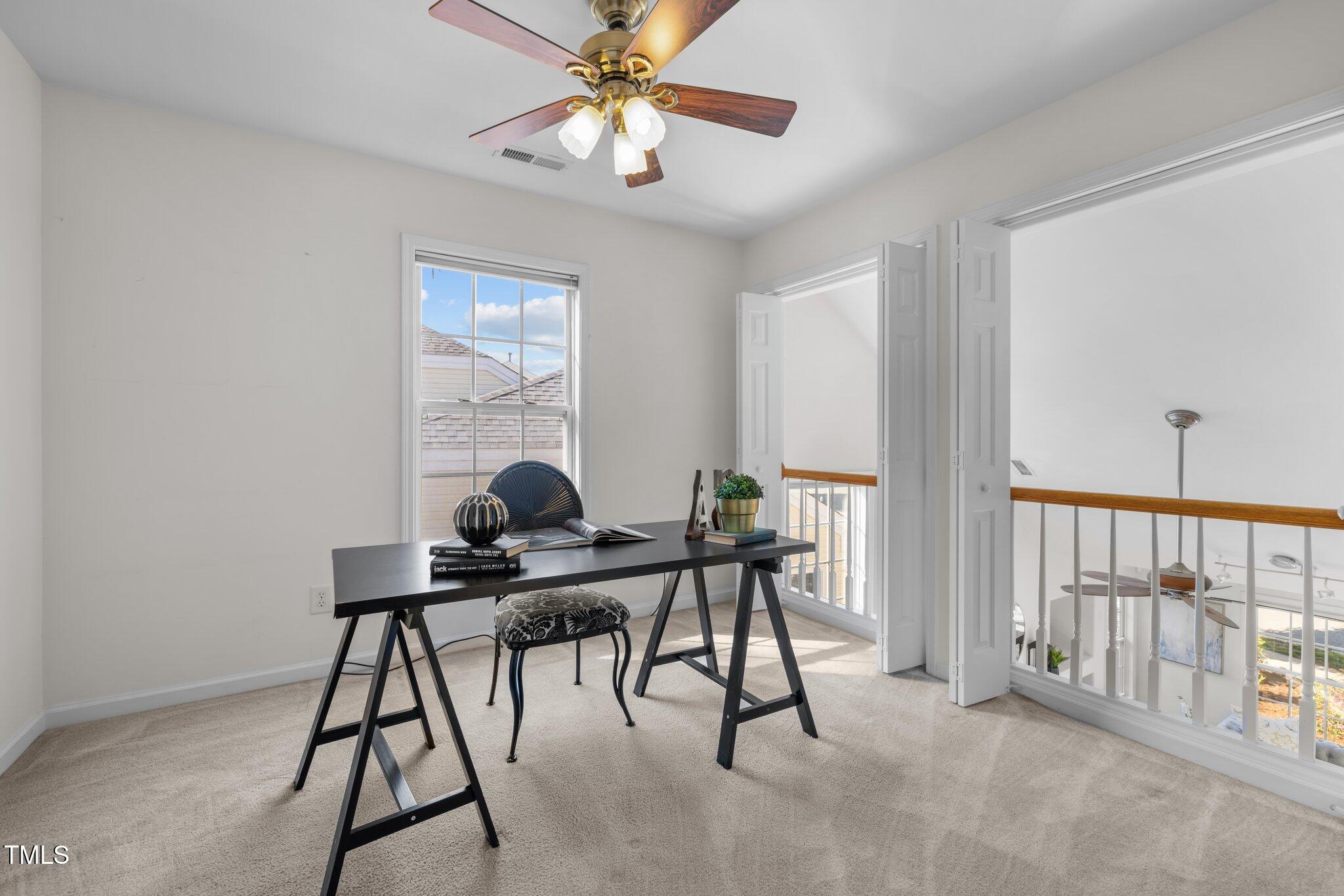 Upstairs home office with a black desk, patterned chair, ceiling fan, and open doors to a landing.