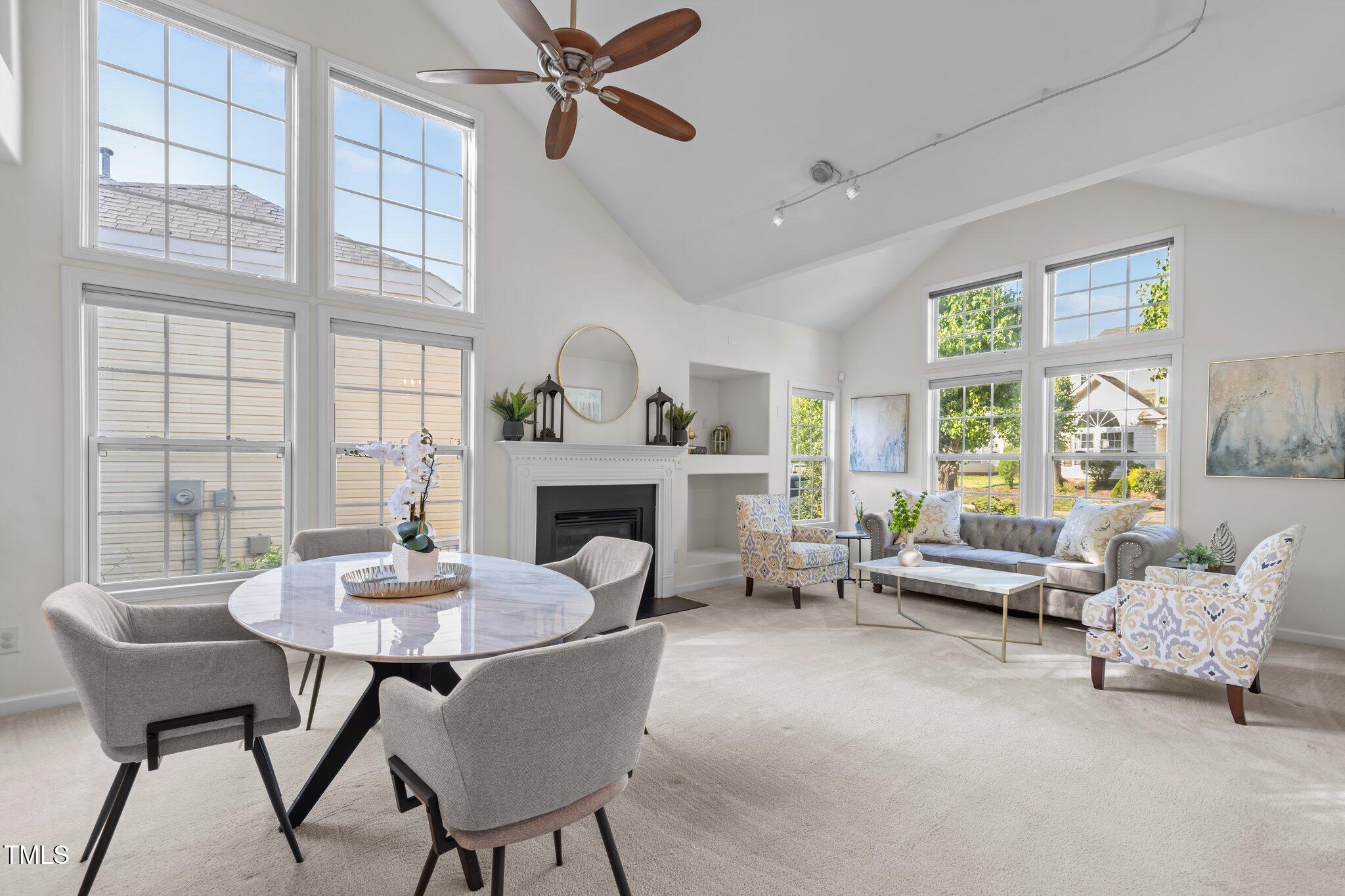 Staged living and dining room with vaulted ceilings, tall windows, and a white fireplace.
