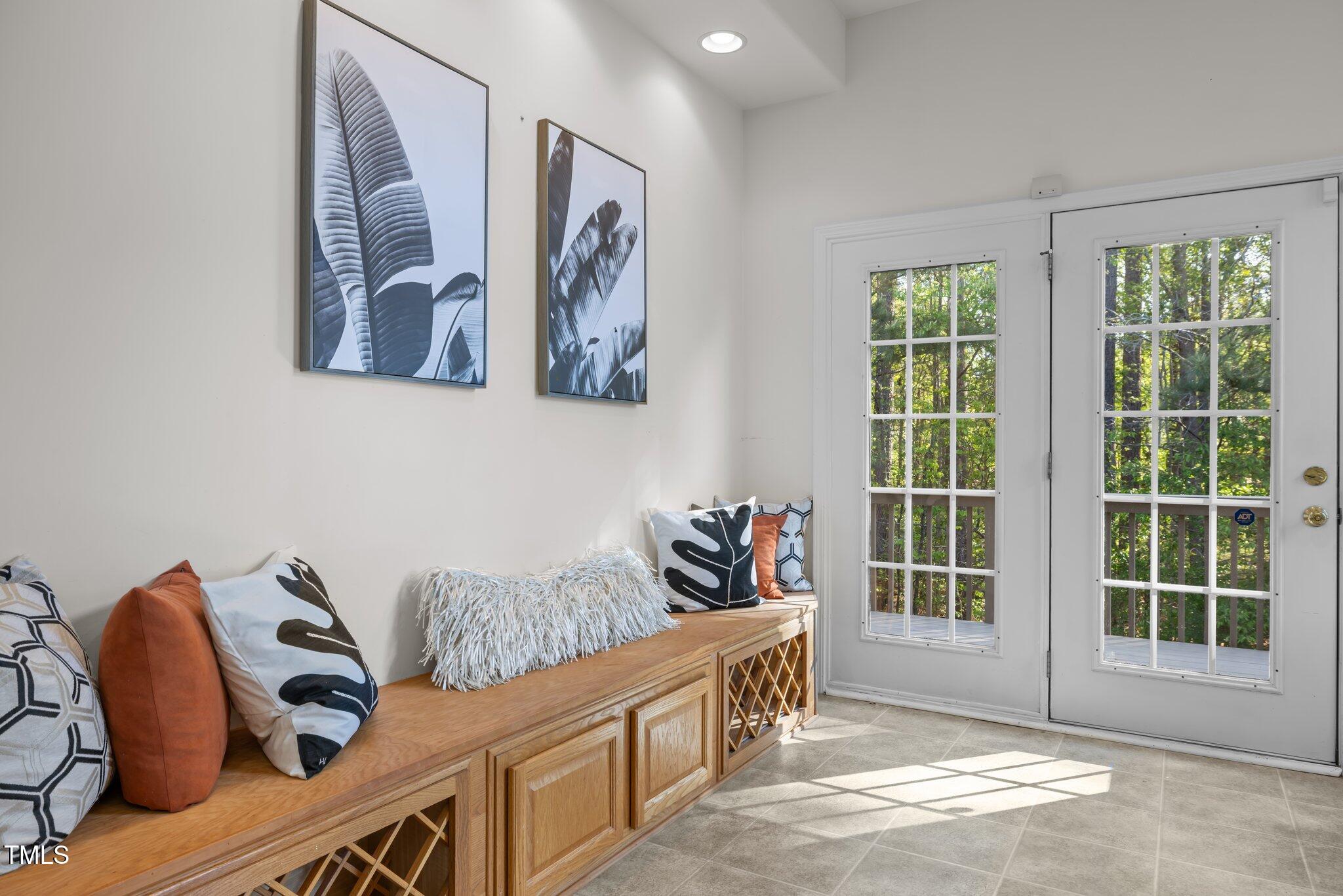 Staged entryway with a built-in wooden bench, patterned cushions, and a glass-paneled door overlooking trees.