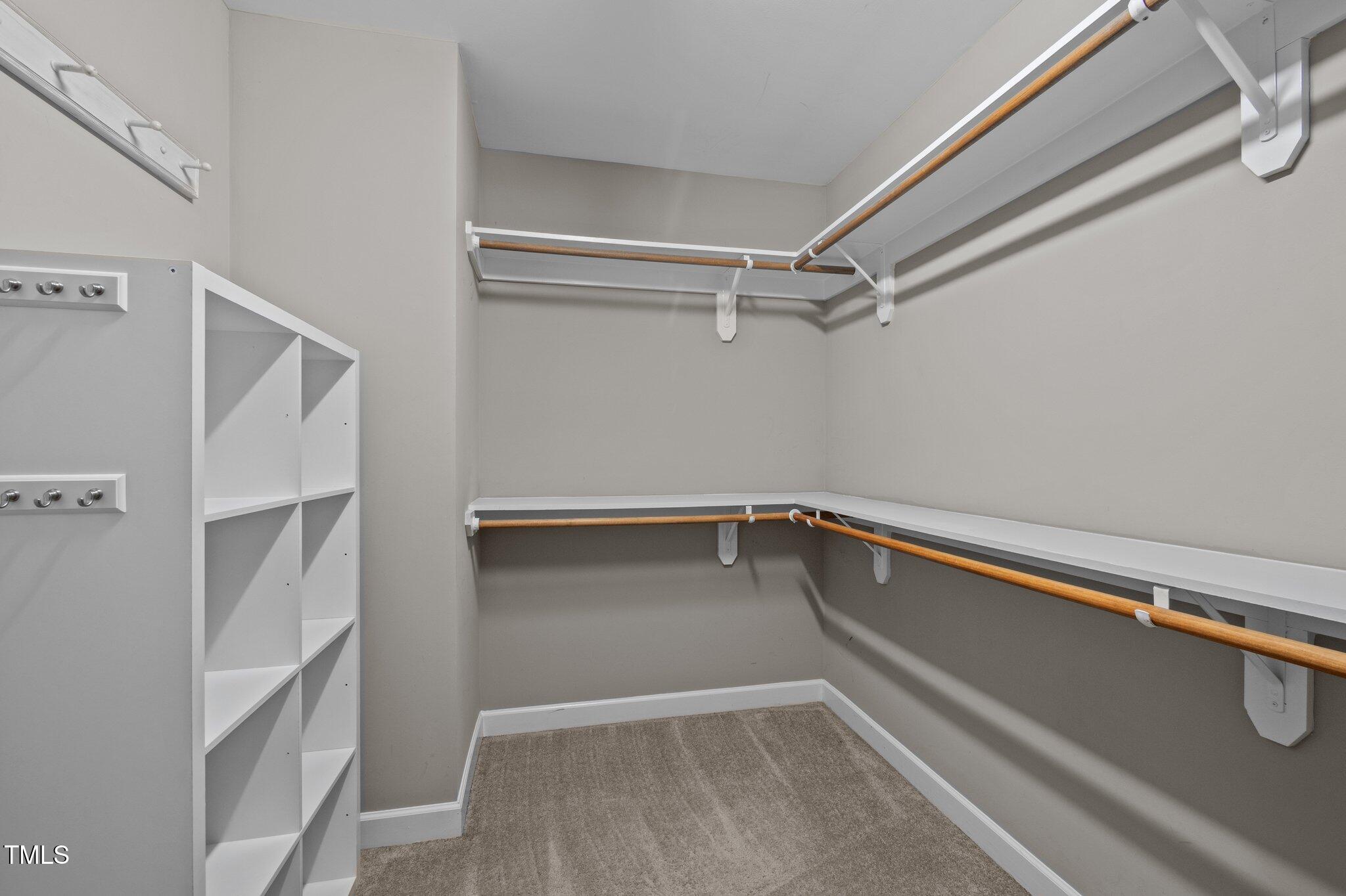 Walk-in closet with white cubby shelves and wooden hanging rods on three walls.