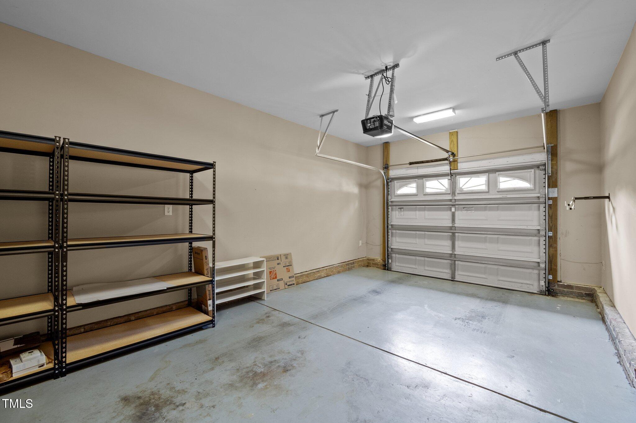 Empty garage with metal shelving, a concrete floor, and a closed sectional door with windows.
