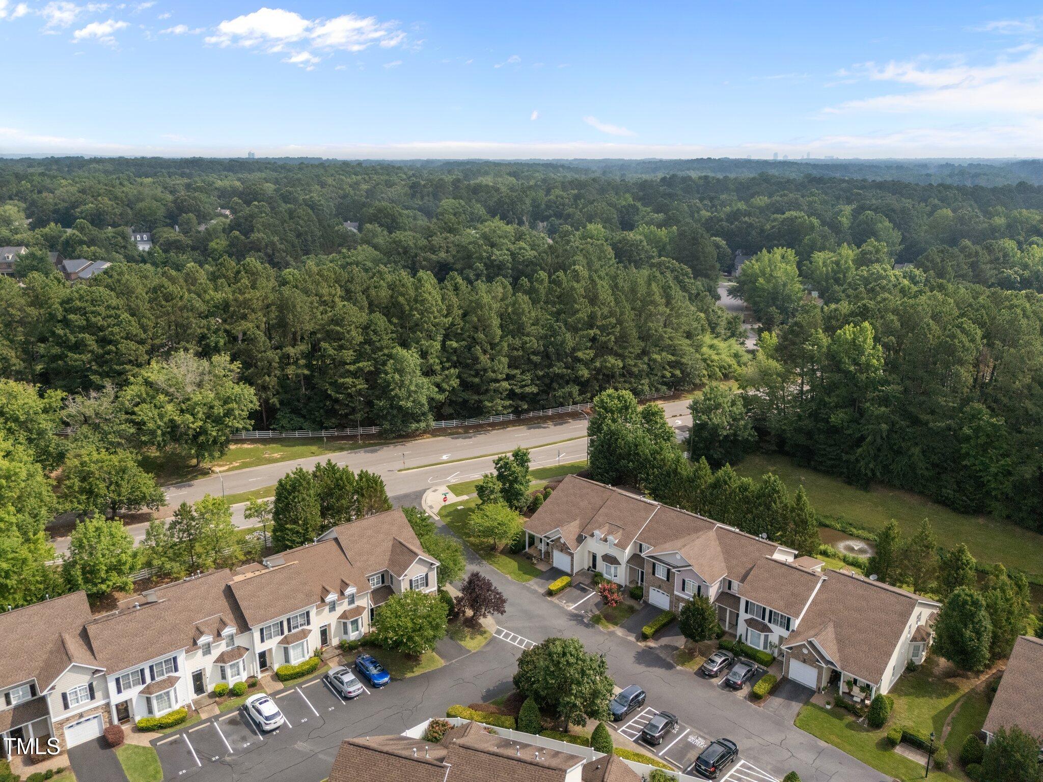 Aerial view of a townhouse community beside a tree-lined road and dense woodland.