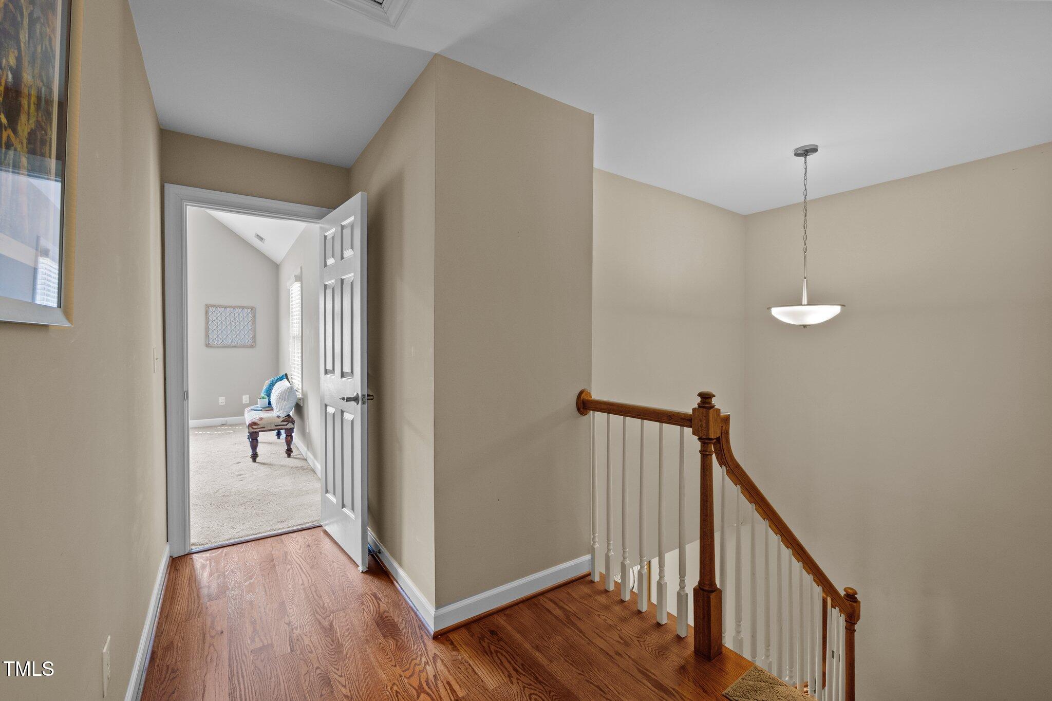 Stair landing with hardwood floors, wooden railing, and an open doorway to a carpeted room.