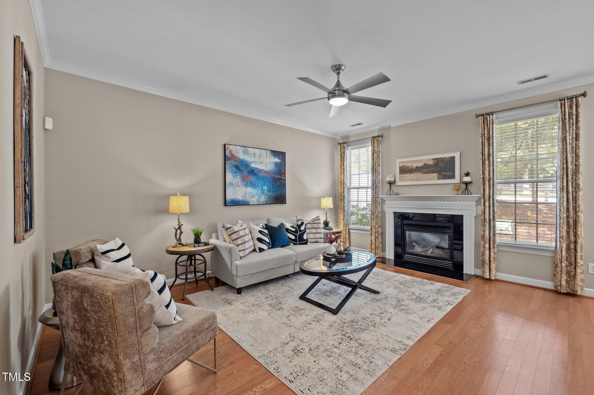 Living room with a white sofa, fireplace, large curtained windows, and hardwood floors.