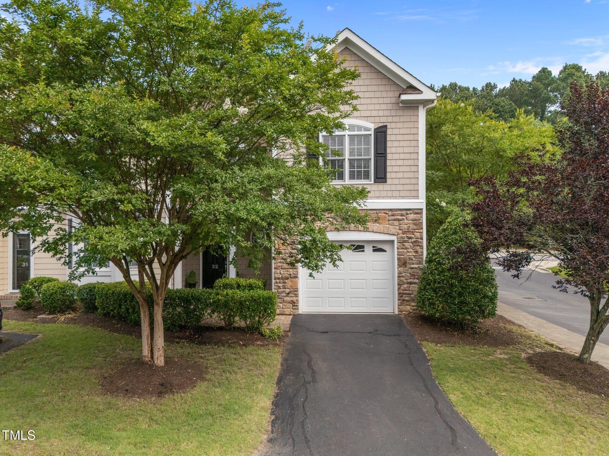 Townhouse exterior with stone veneer, white garage door, driveway, and leafy landscaping.