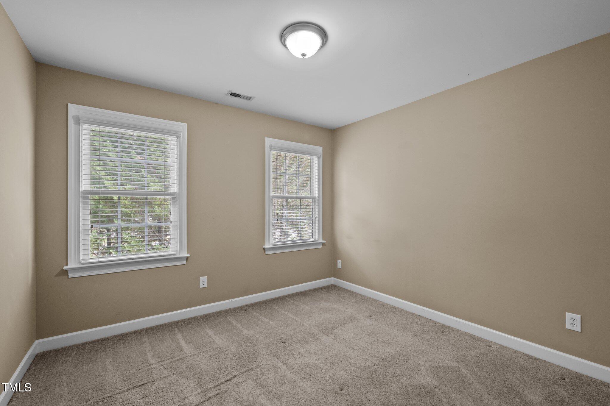Empty bedroom with gray carpet and two windows with white blinds.