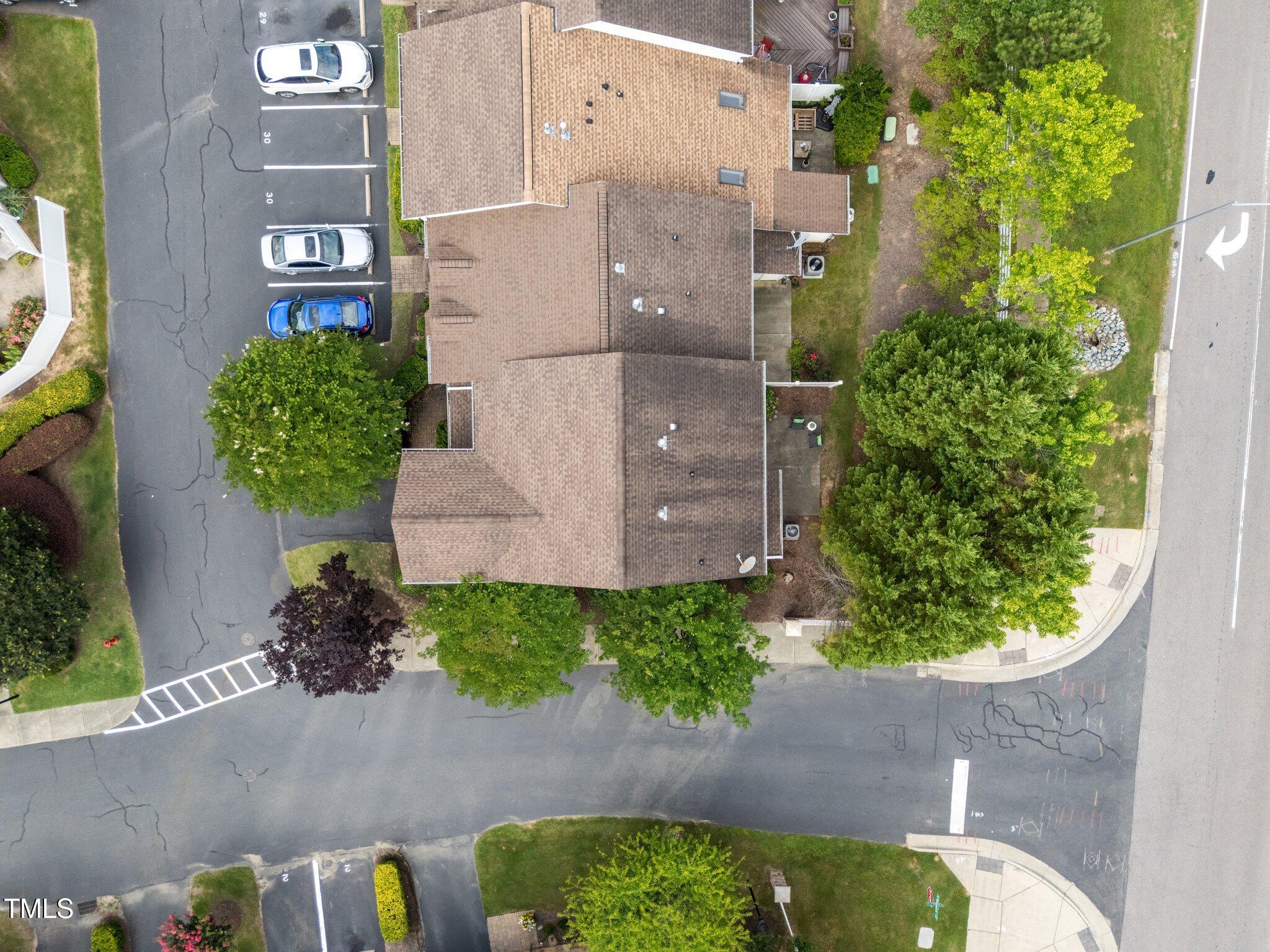 Aerial view of attached homes with tan roofs, parking spaces, and mature trees.