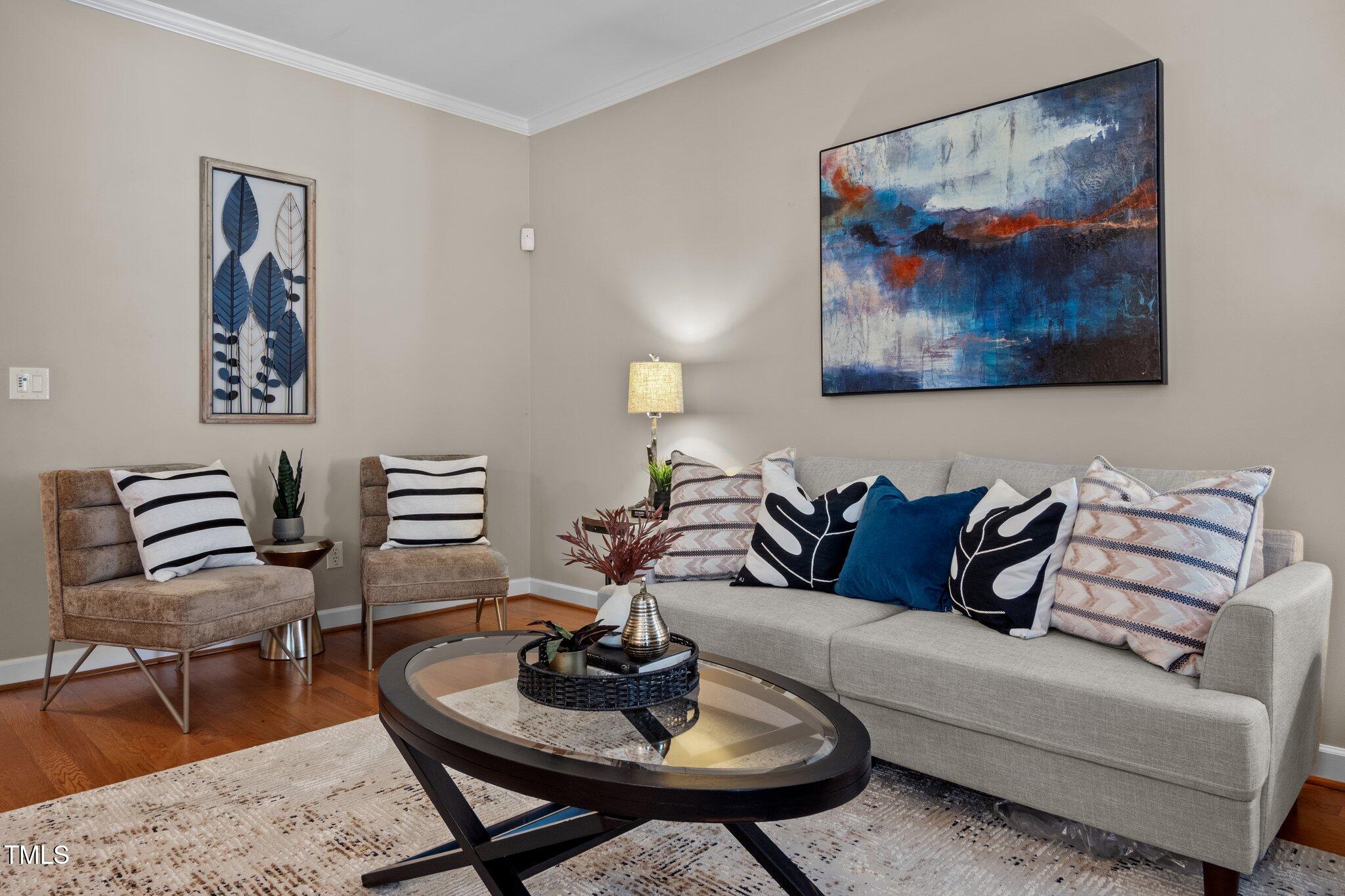 Living room with a gray sofa, two chairs, an oval glass coffee table, and colorful abstract wall art.