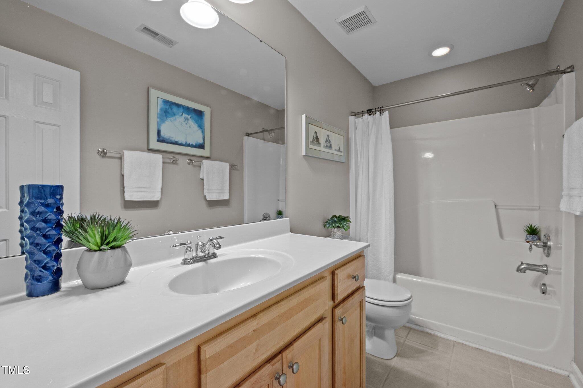 Bathroom with a wood vanity, large mirror, and white tub-shower combination.