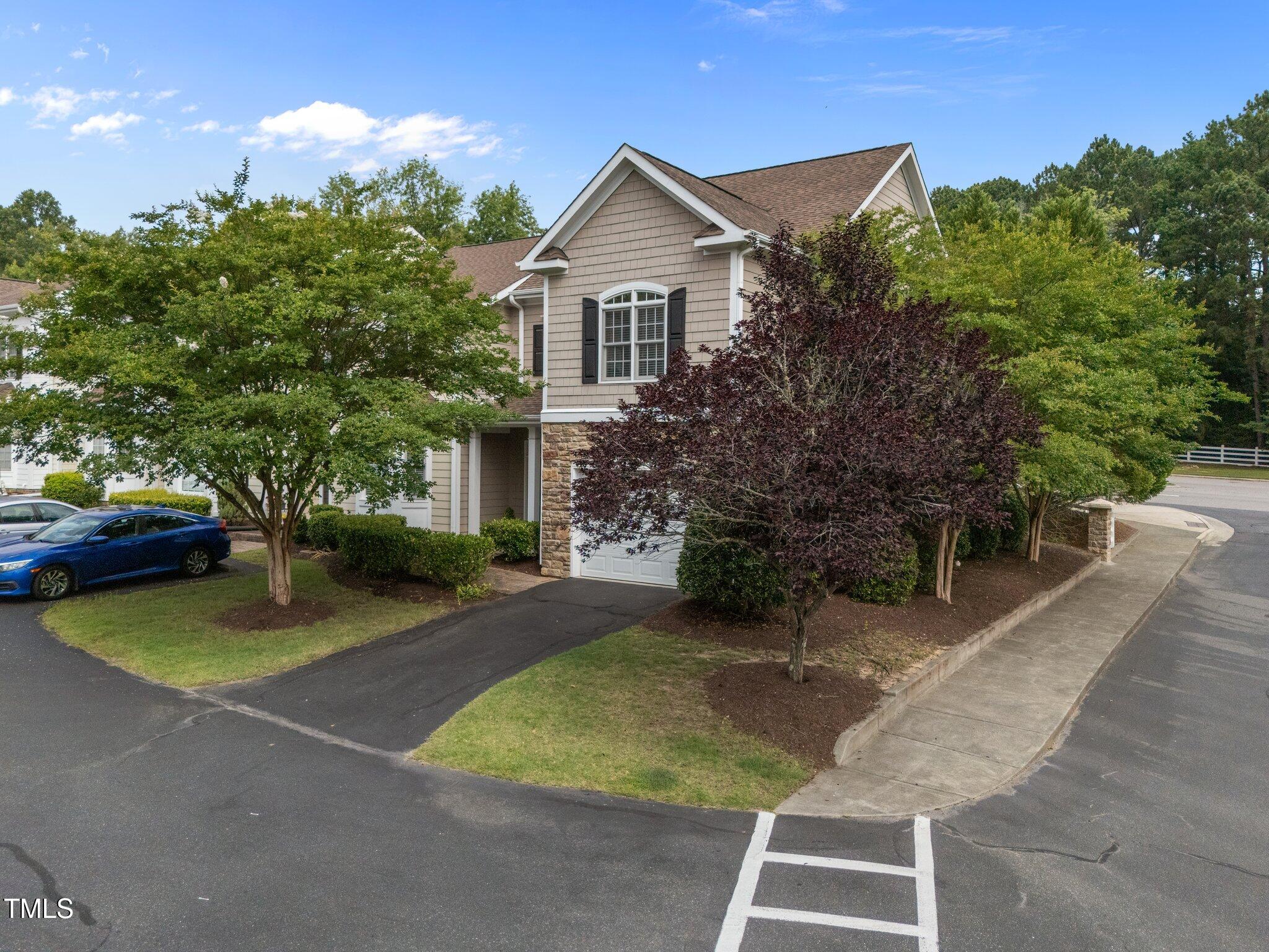 Two-story beige home with stone-accented garage, landscaped trees, and a driveway.