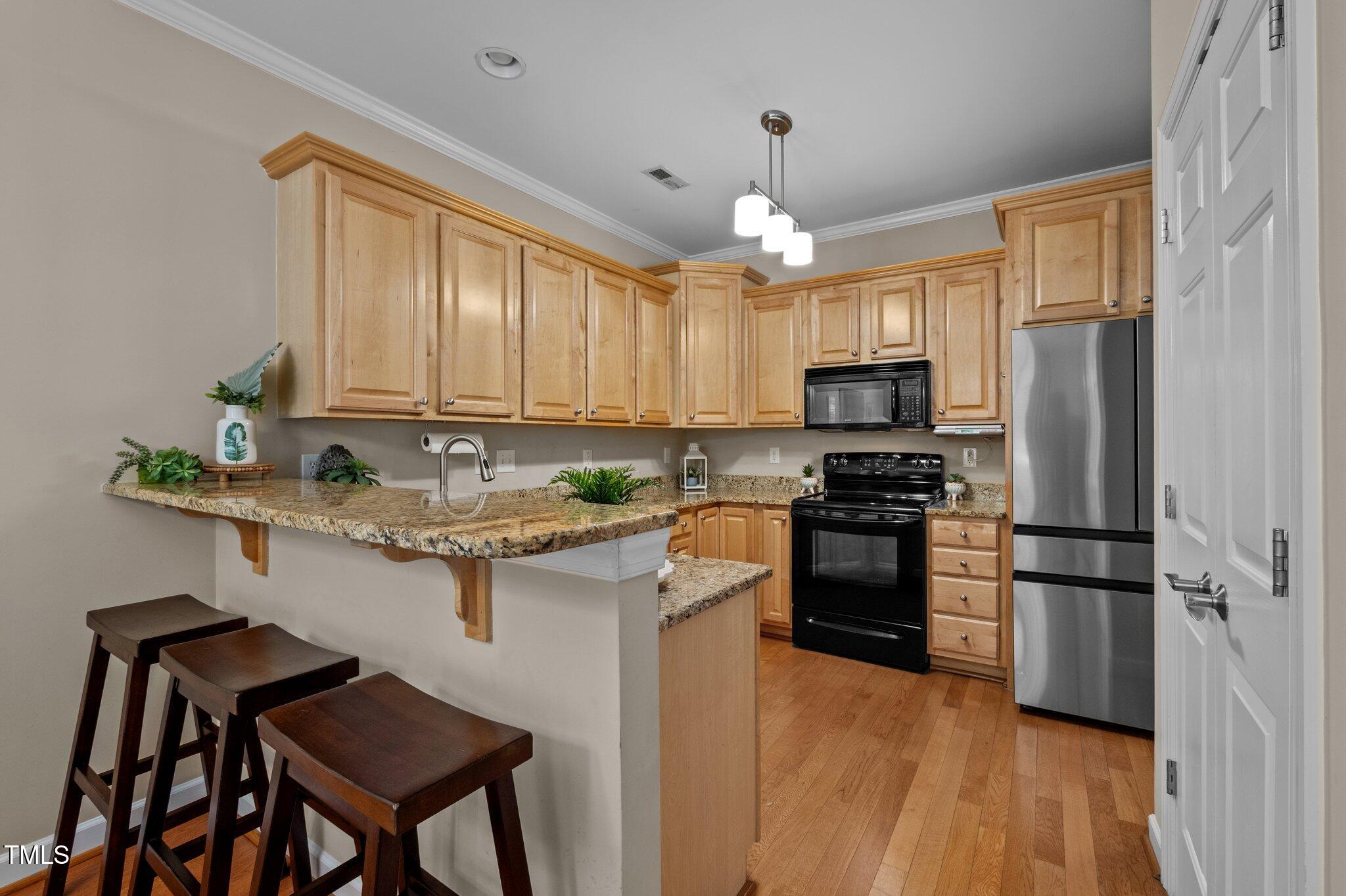 Kitchen with wood cabinets, granite counters, breakfast bar, and stainless steel refrigerator.