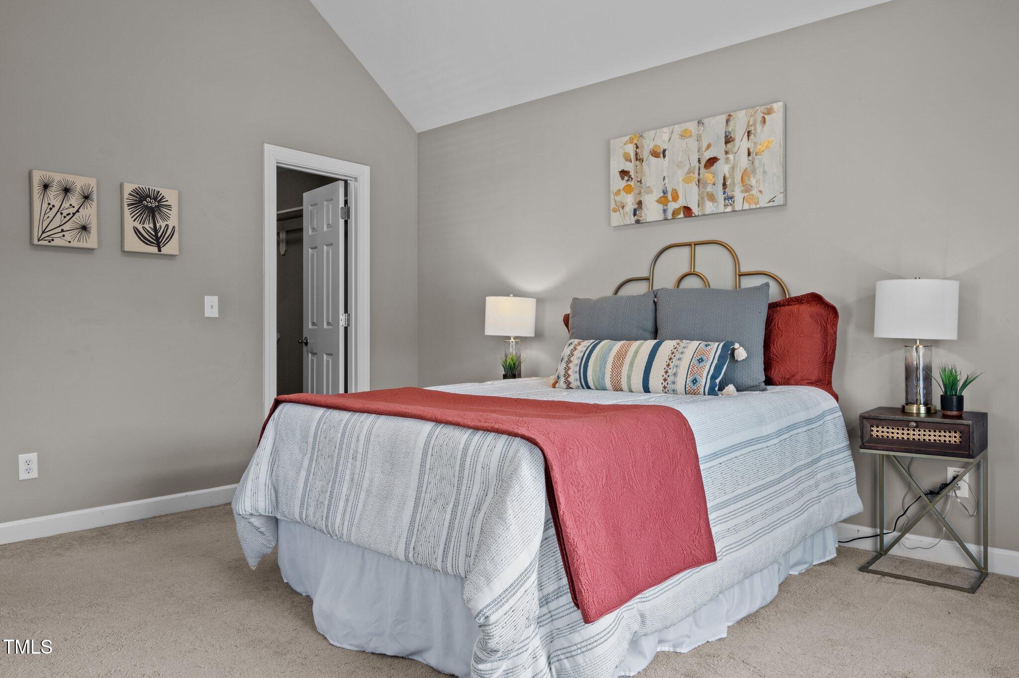 Staged bedroom with striped bedding, a coral-red quilt, and a brass-toned headboard.