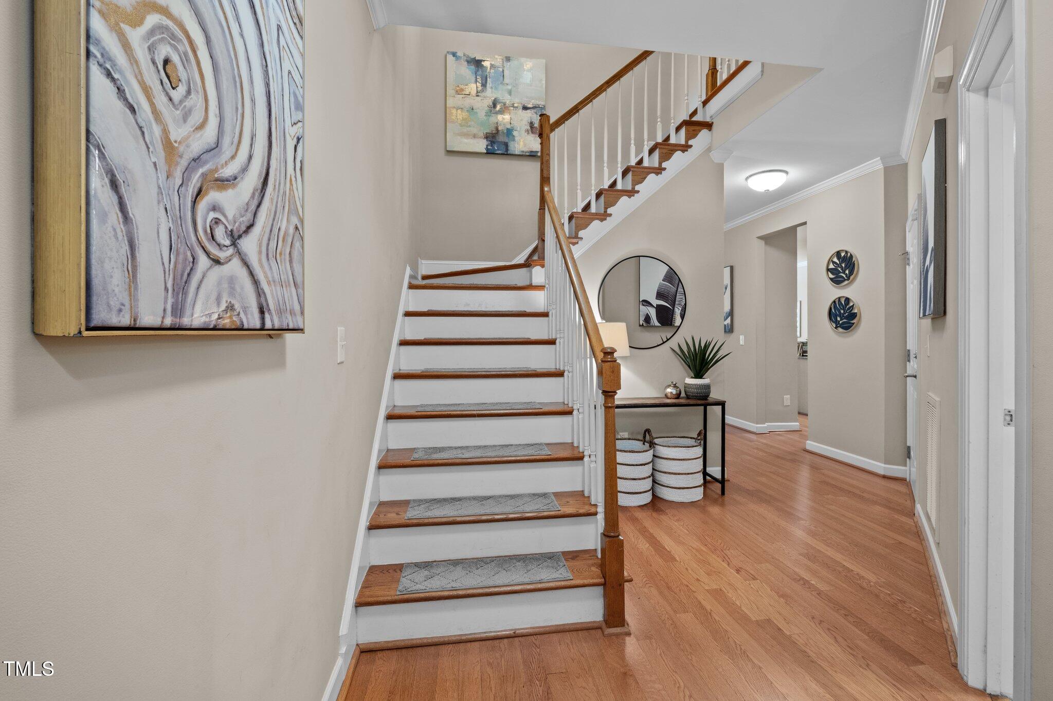 Entryway with a wood-and-white staircase, hardwood floors, and a console table beneath a round mirror.