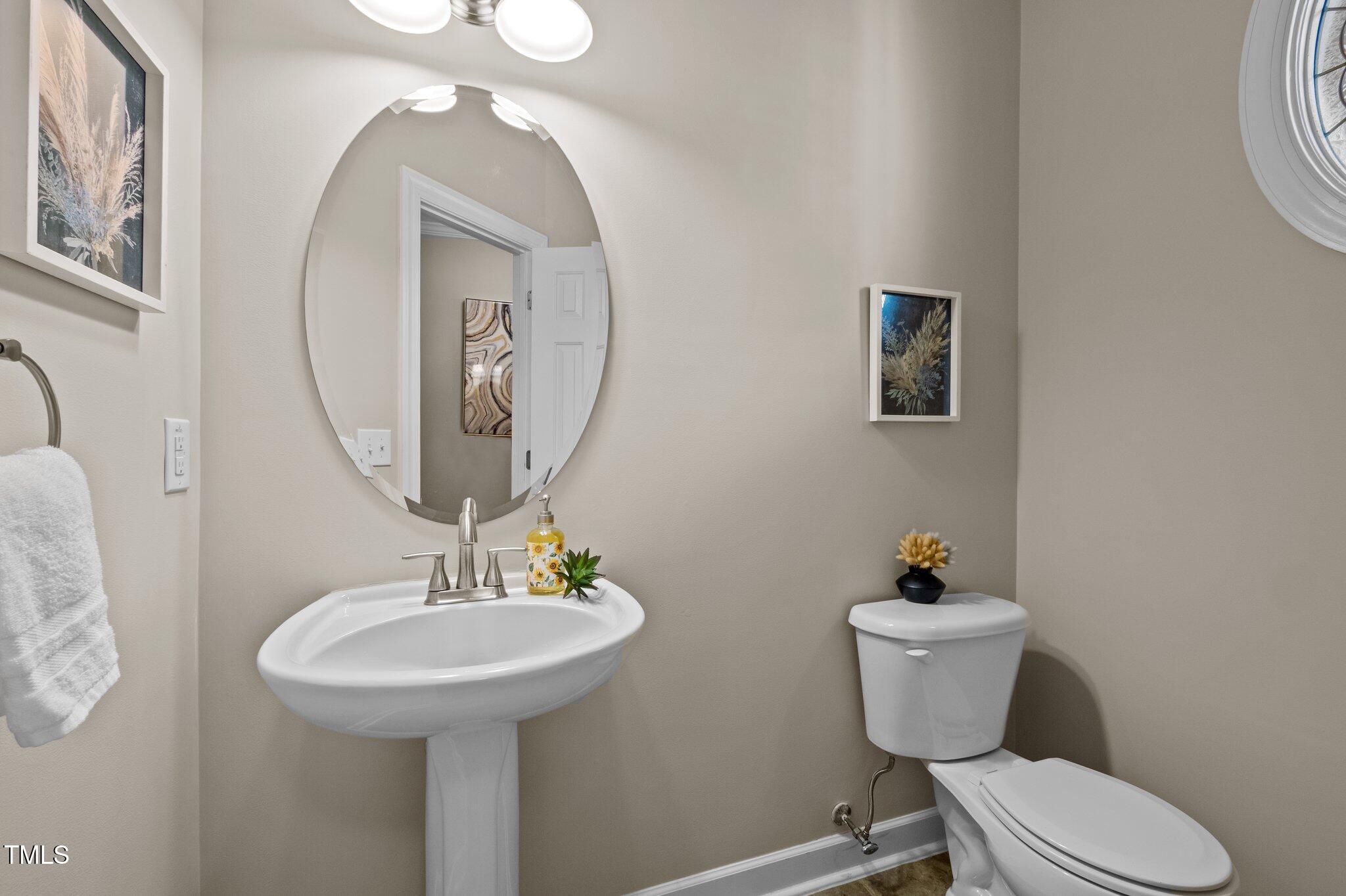 Half bathroom with a pedestal sink, toilet, oval mirror, and round window.