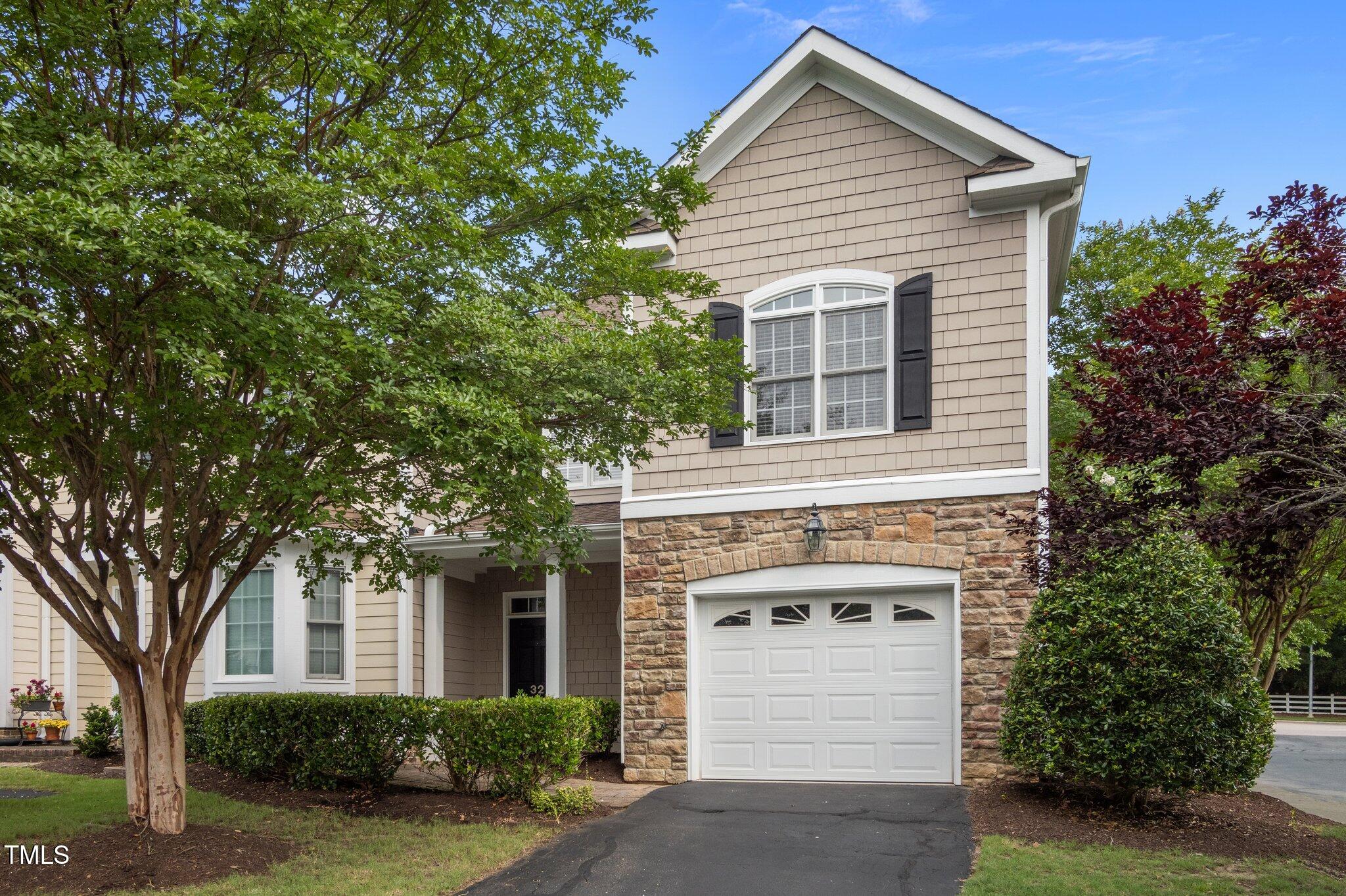 Two-story townhouse with stone facade, attached garage, and leafy landscaping.