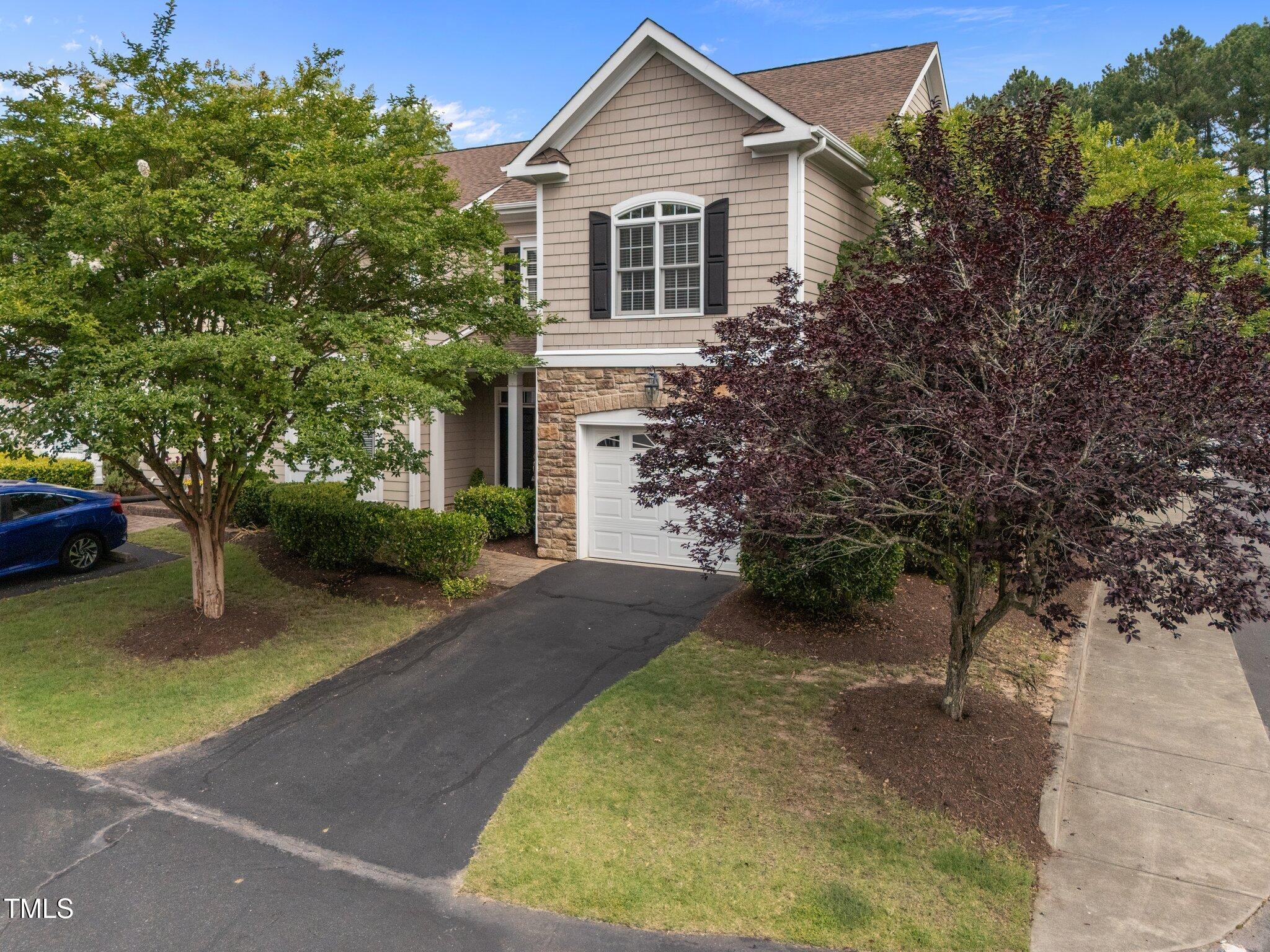 Two-story home with stone accents, a white garage door, and a tree-lined driveway.