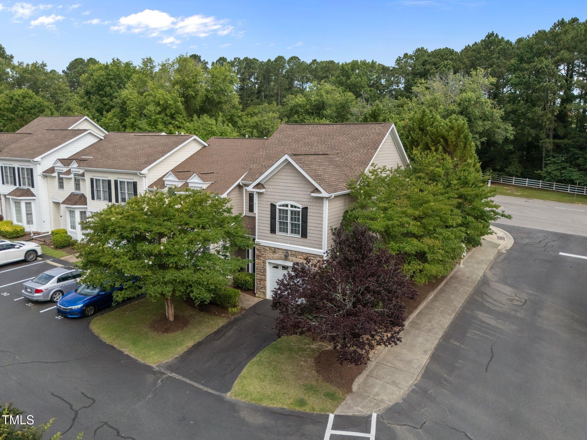 Aerial view of attached homes beside parking spaces, sidewalks, and wooded grounds.
