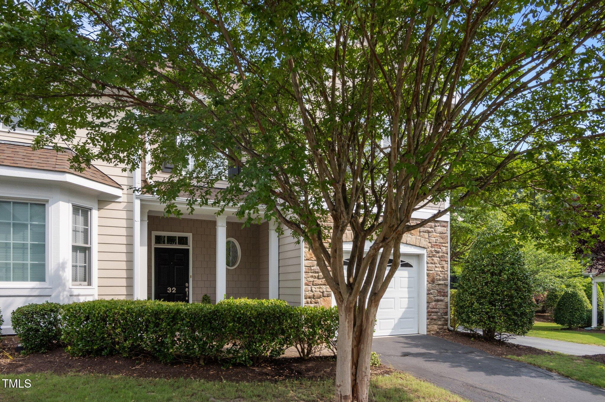 Home exterior with a black entry door, stone-accented garage, and large leafy tree.