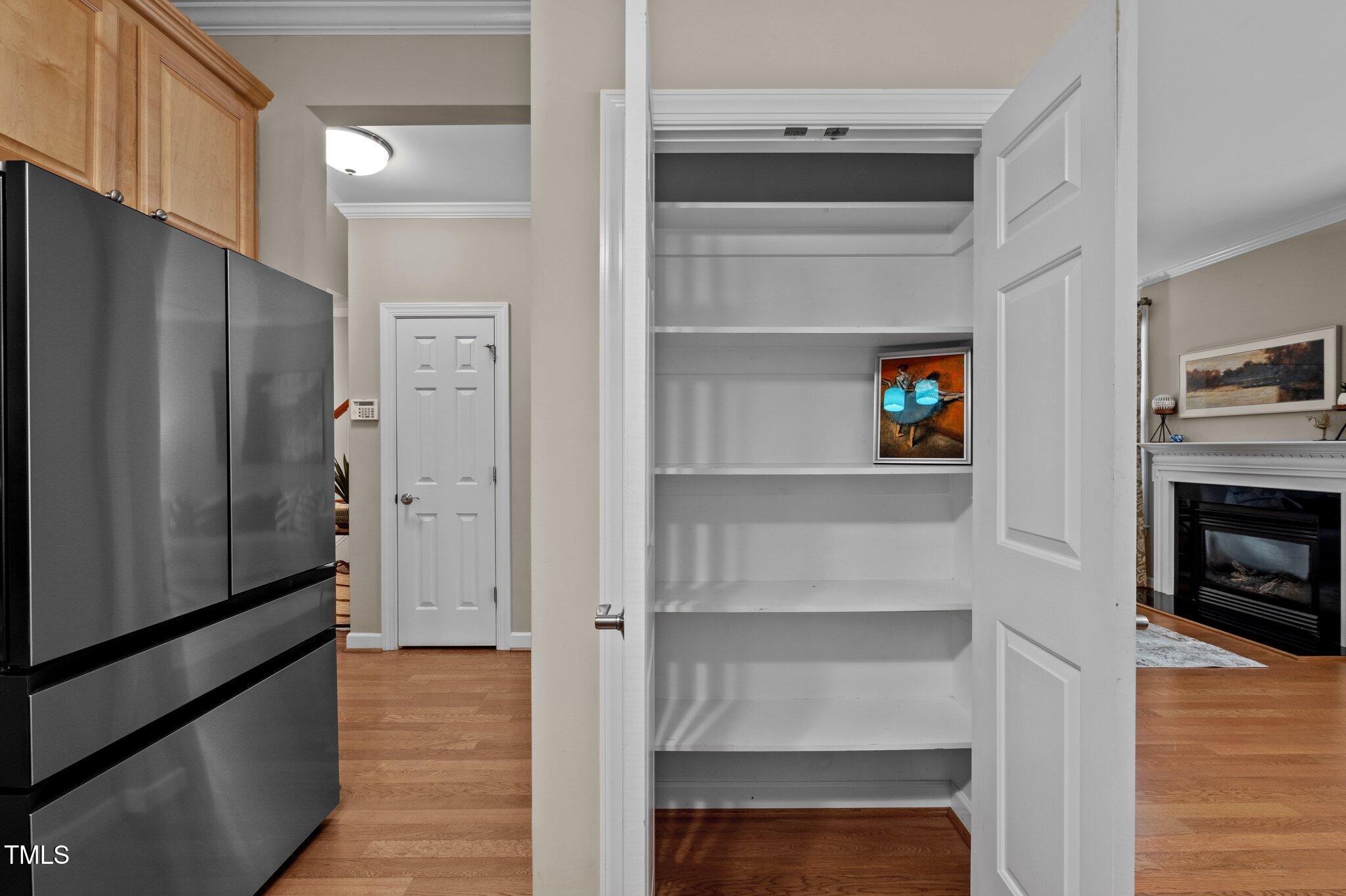 Open pantry with white shelves beside a dark refrigerator and wood kitchen cabinets.