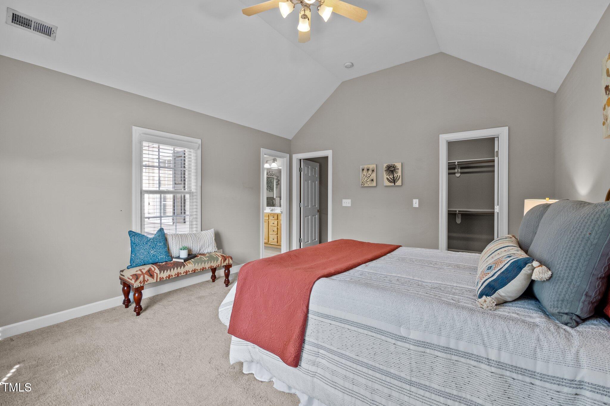 Bedroom with a vaulted ceiling, striped bedding, coral throw, window seat, and open closet.