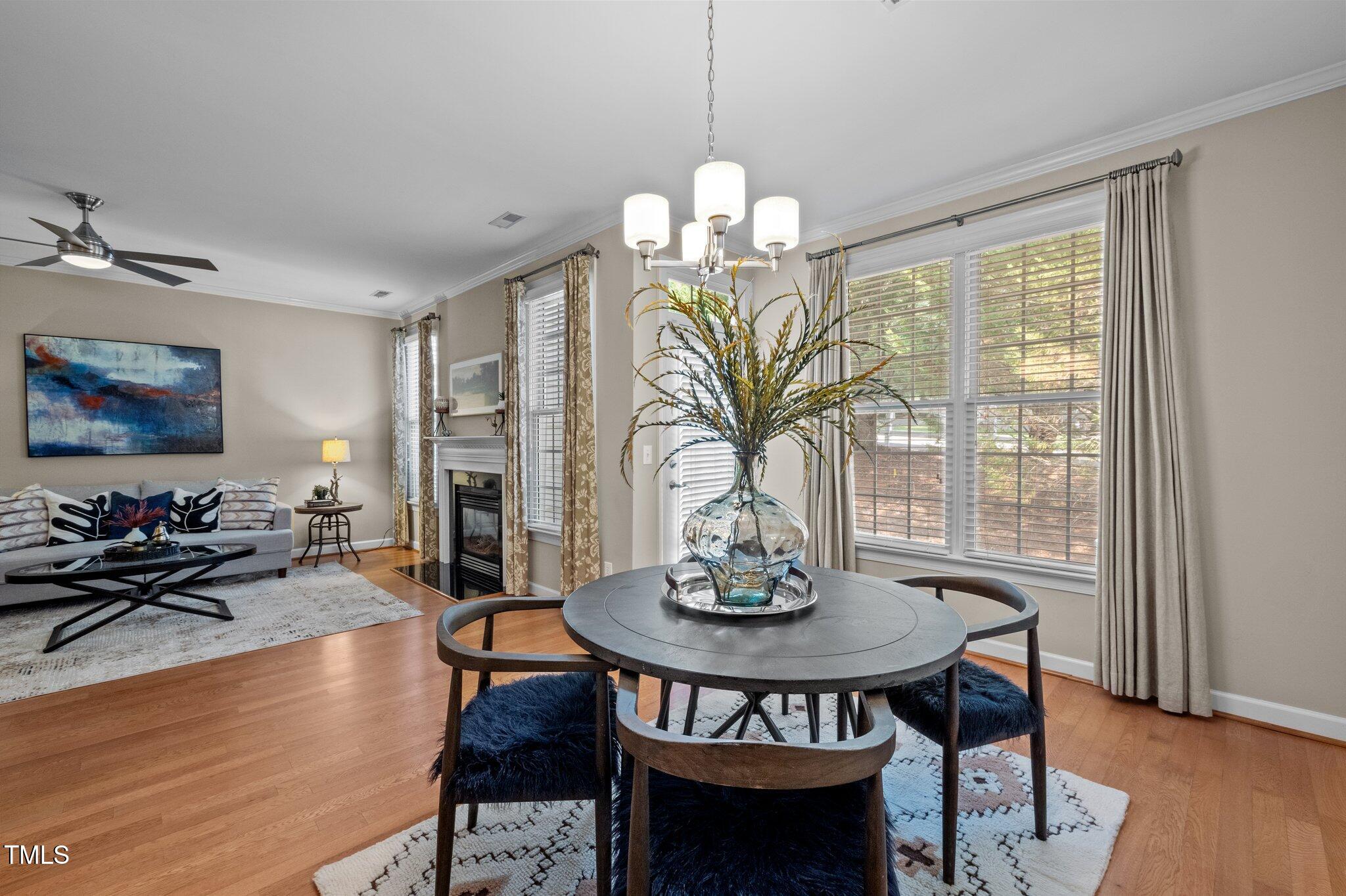 Staged dining and living room with a round table, fireplace, gray sofa, and large windows.