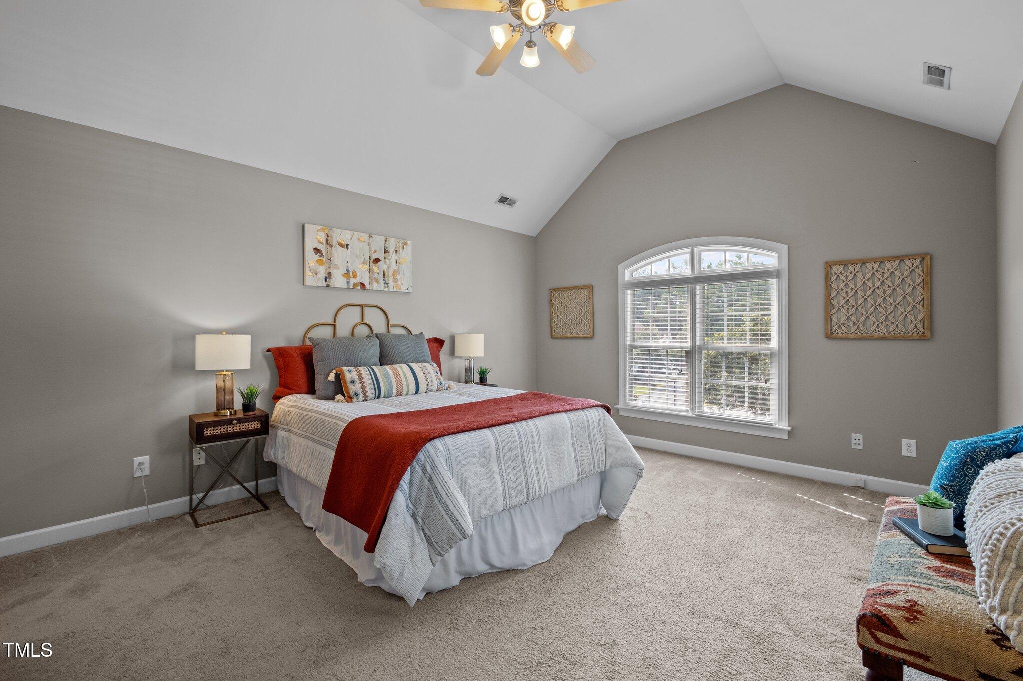Furnished bedroom with vaulted ceiling, arched window, and bed with a rust-red throw.