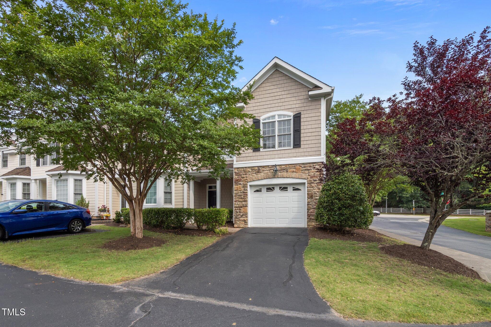 Townhouse exterior with stone facade, attached garage, and tree-shaded driveway.