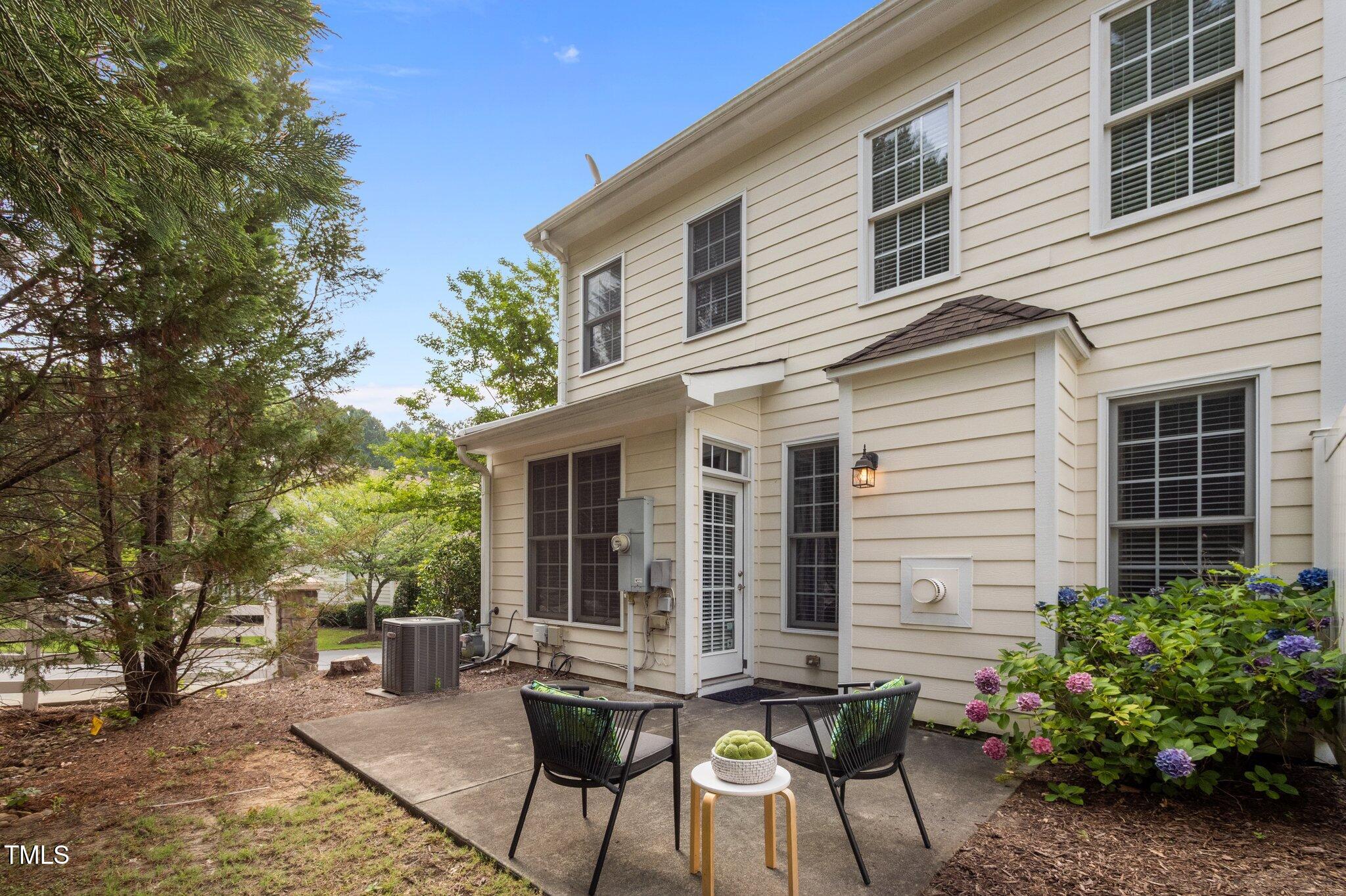 Home’s concrete patio with black chairs, a small table, and blooming hydrangeas beside the house.