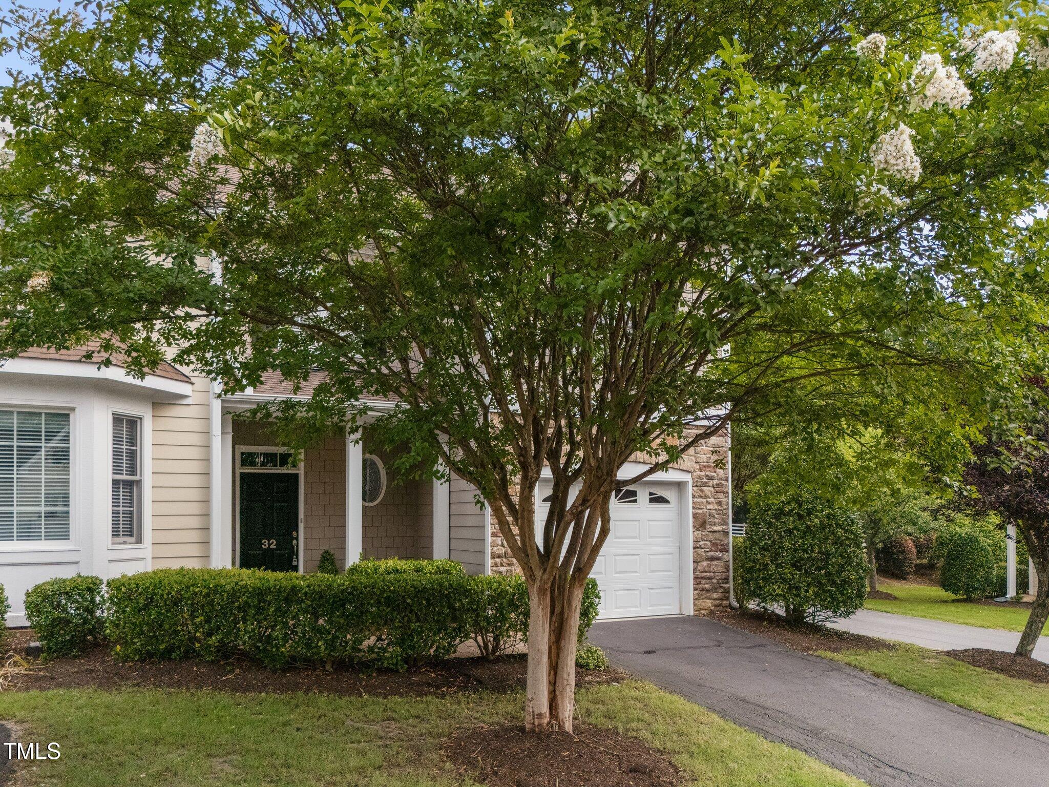 Home entrance and garage partly shaded by a mature flowering tree, with unit number 32 on the front door.